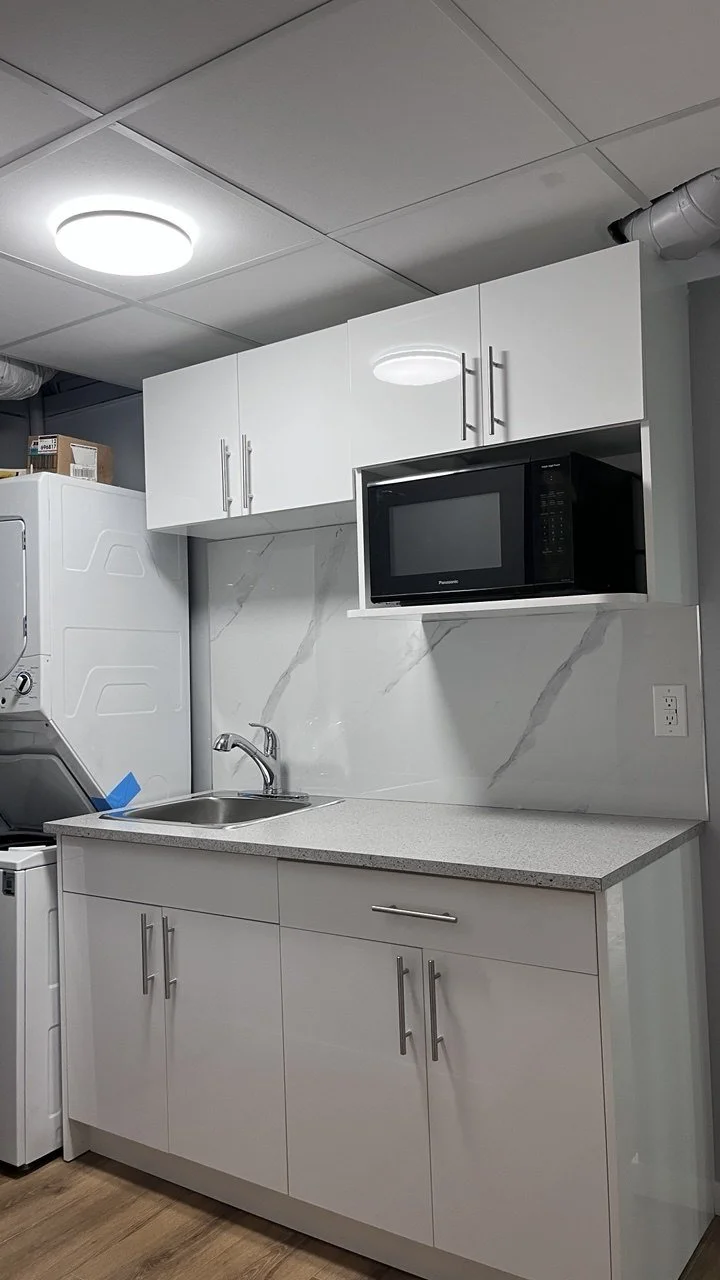 Kitchen with white cabinets, a black microwave, a small countertop with a sink, and a white marble backsplash.