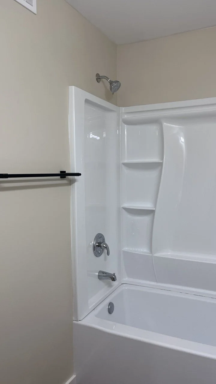 White bathtub with built-in shelves, showerhead, and faucet in a bathroom with beige walls.