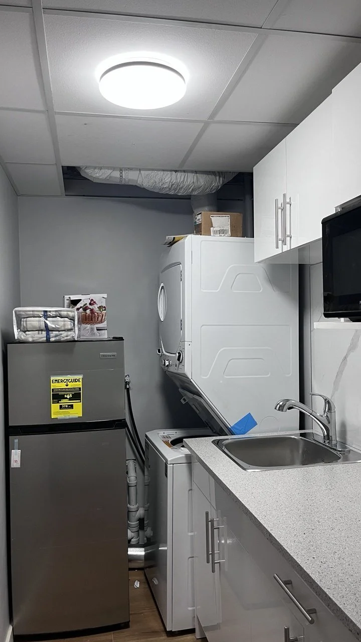 Small laundry room with washing machine and dryer stacked, white cabinets, sink, microwave, and a small refrigerator with an 'Energy Guide' label.