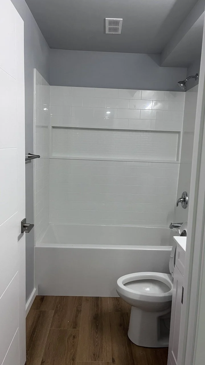 Bathroom with a bathtub, showerhead, toilet, and wooden floor and gray walls.