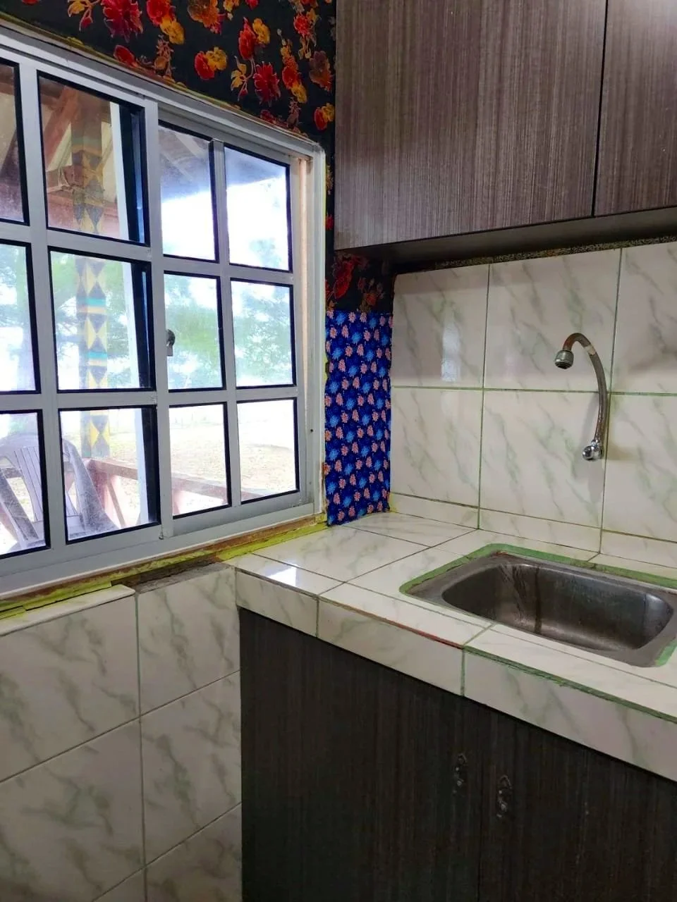 Kitchen with a sink, tiled counter, window with decorative curtains, and wall tiles.