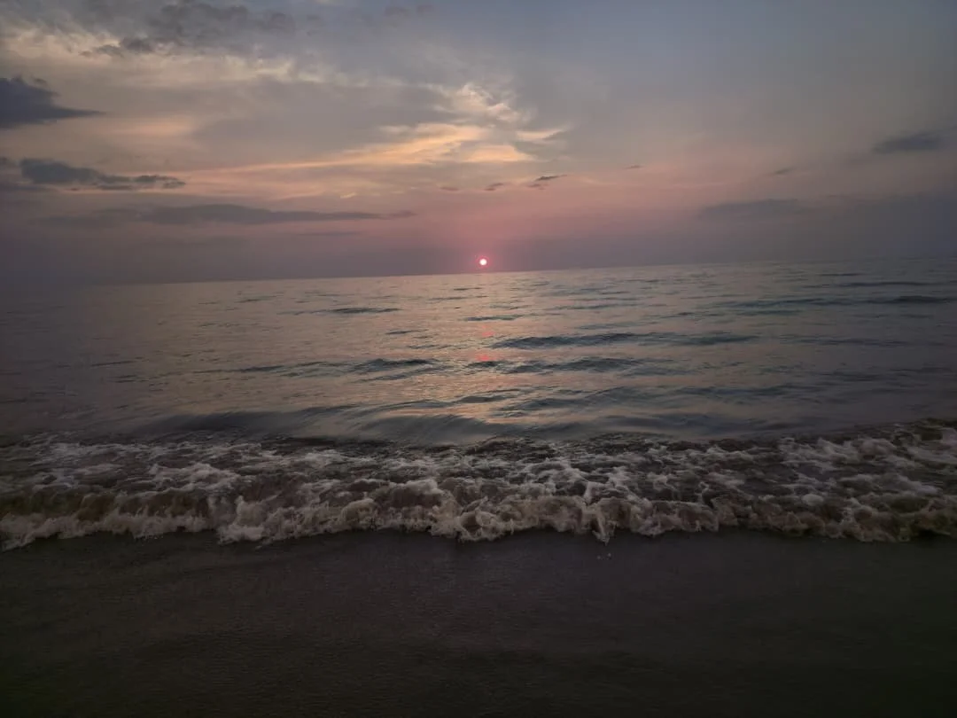 Sunset over the ocean with partly cloudy sky and gentle waves hitting the beach.
