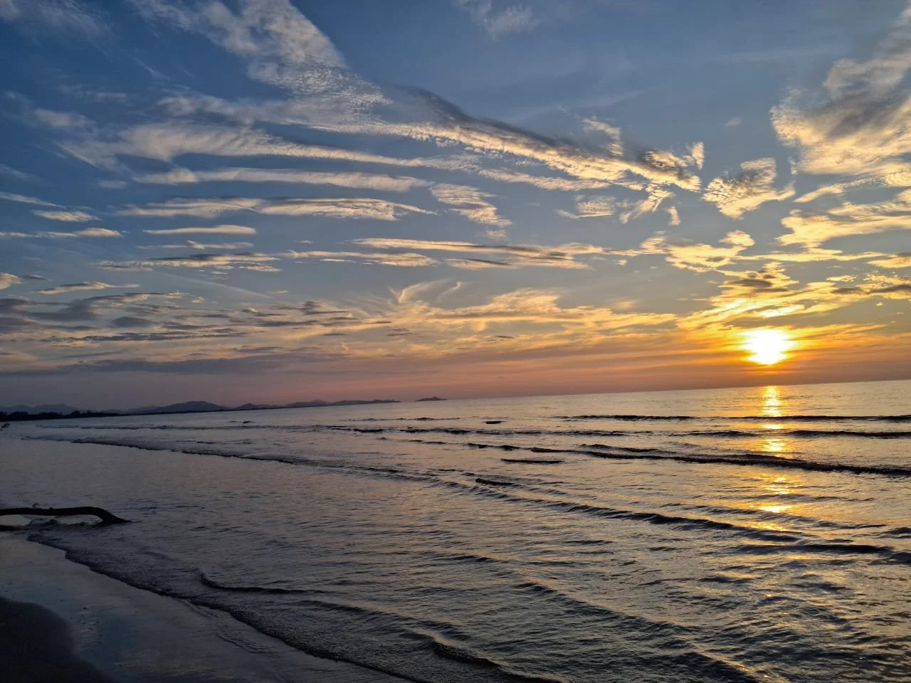 Sunset over a calm ocean with gentle waves and a partly cloudy sky.