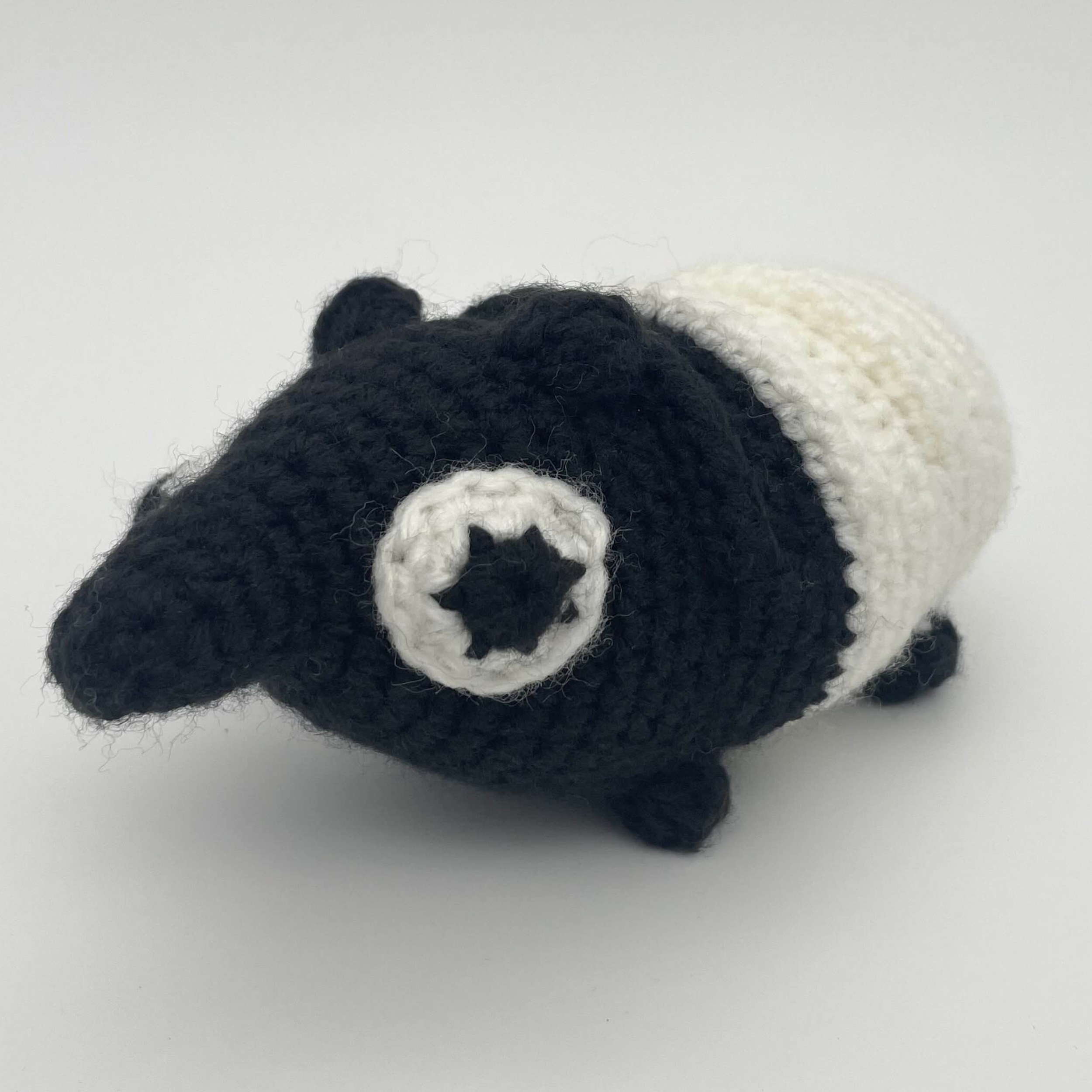 Black and white crocheted tapir plush with a rounded body, short legs, small ears, and a star-shaped eye detail, photographed against a light background.