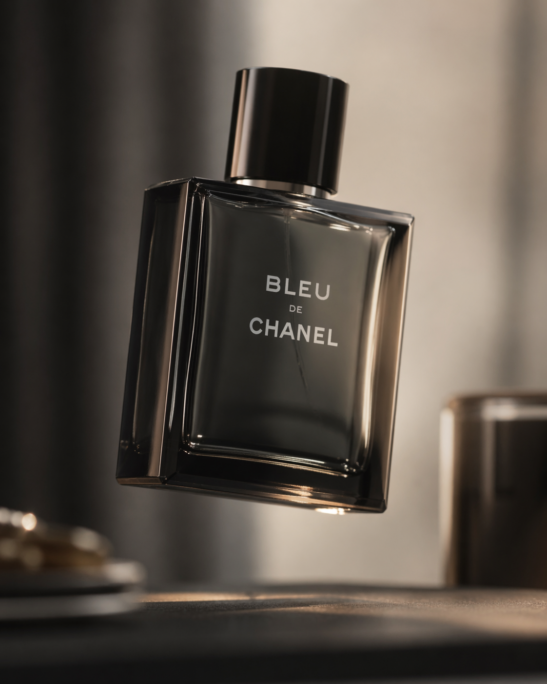 A bottle of Bleu de Chanel perfume floating in mid-air, with a black cap and clear glass body, displaying the brand name in white text.