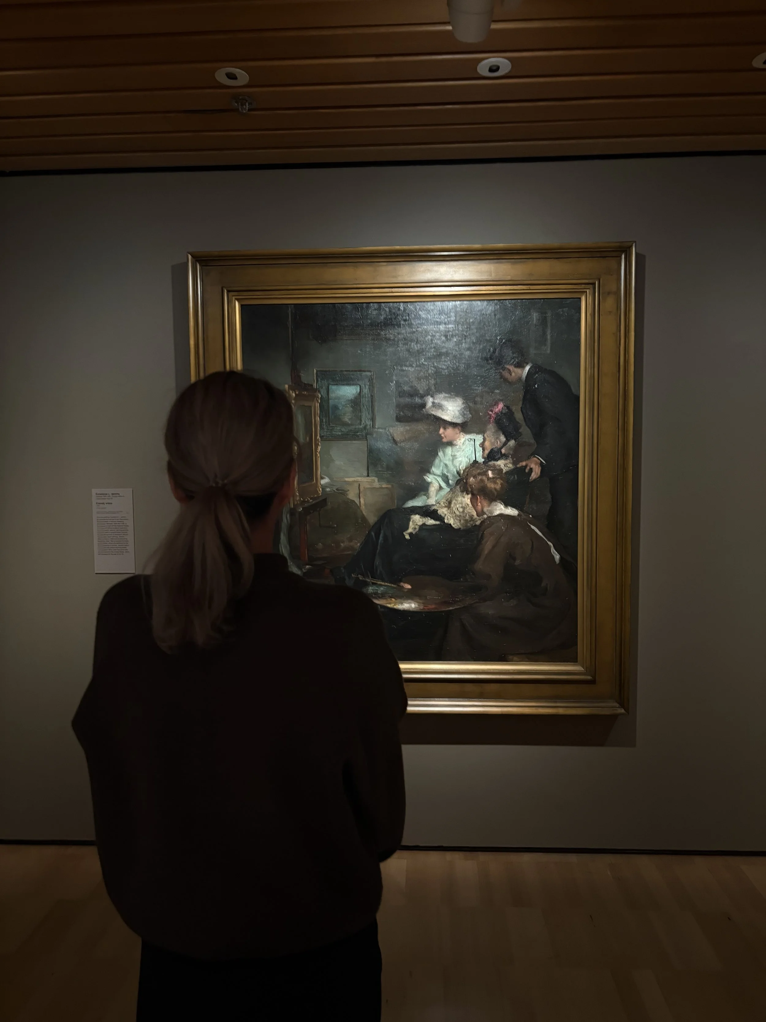 A woman is viewing a landscape painting in an art gallery.