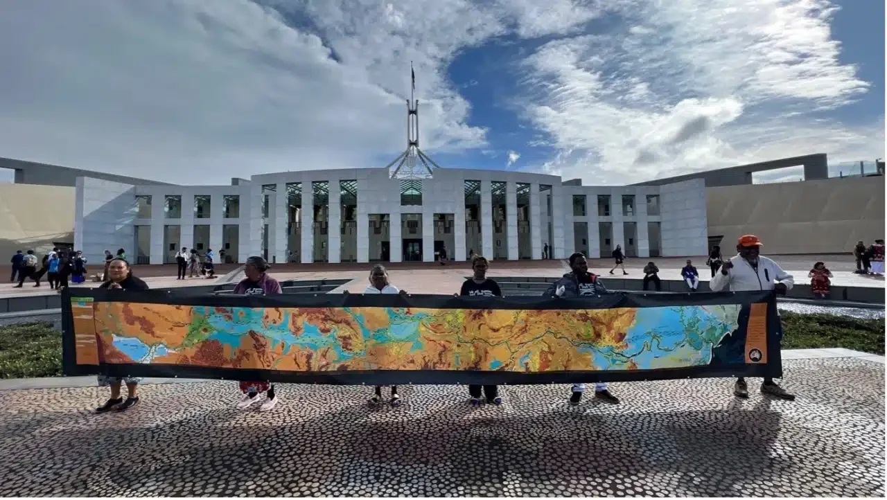 People holding a large map in front of the Australian Parliament House.
