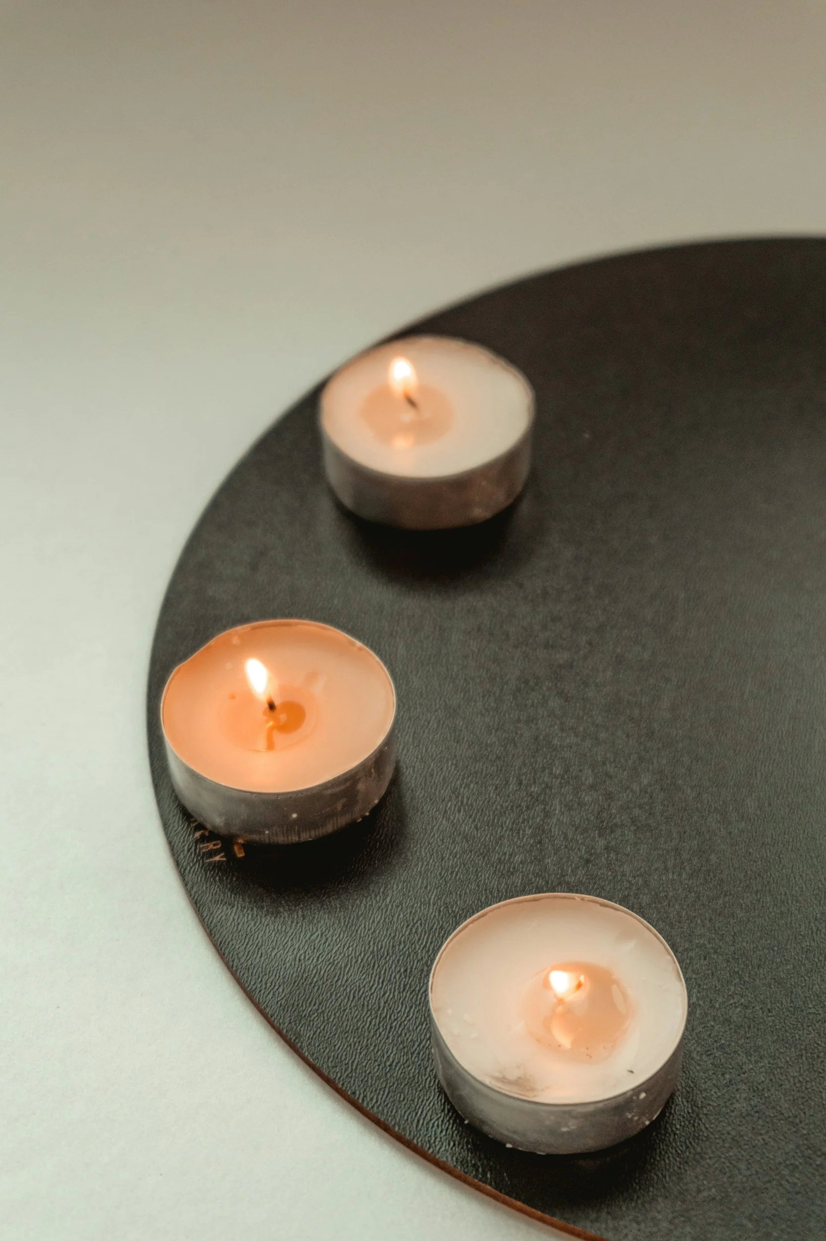 Candles on a round black tray on a white surface.
