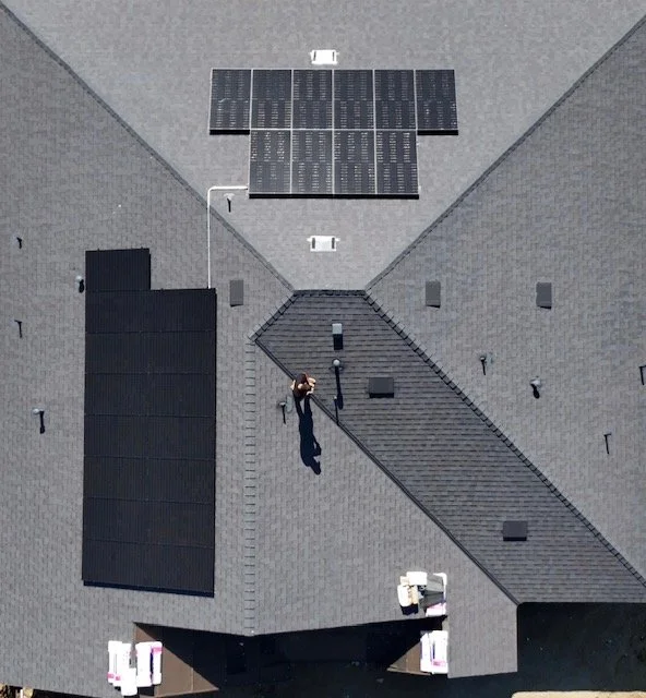 An aerial view of a gray roof with solar panels, a person walking on a dividing ridge, and vents or vents on the roof.