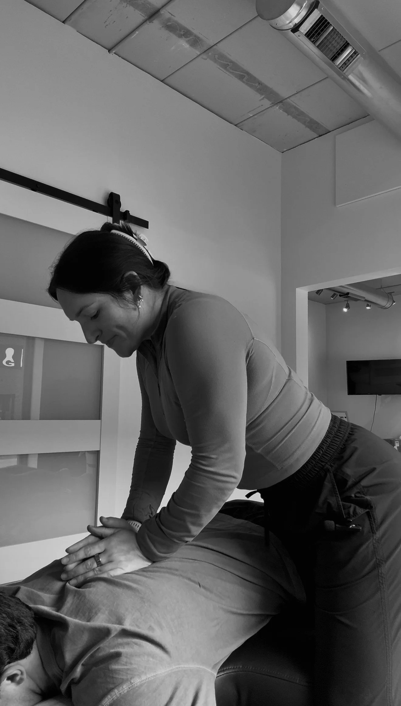 A woman providing chiropractic care to a person lying face down on a treatment table in a medical office.