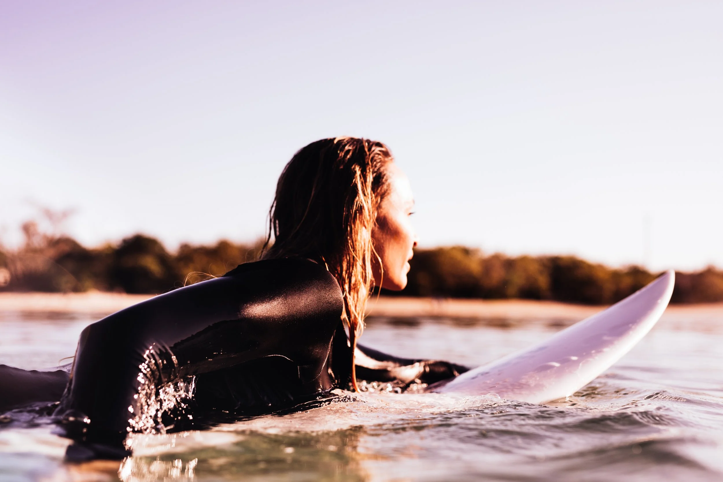 A woman paddling a surfboard at sunrise wearing a black wetsuit on the Gold Coast