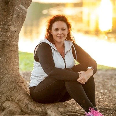 Woman sitting by a tree with a lake in the background during sunset
