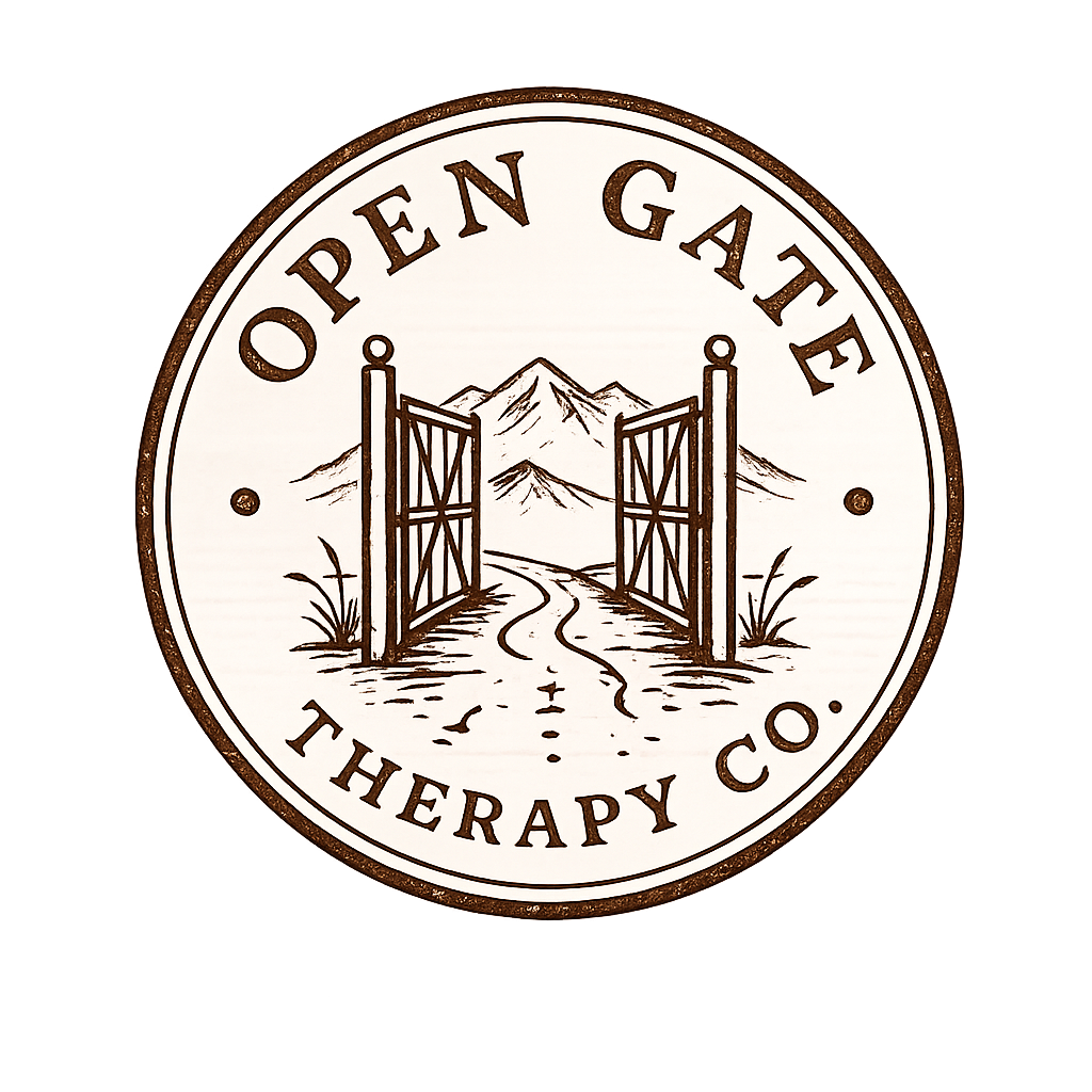 A circular sign for a therapy company called 'Open Gate Therapy Co.' featuring an illustration of open gates leading to mountains, a dirt road, and some grass.
