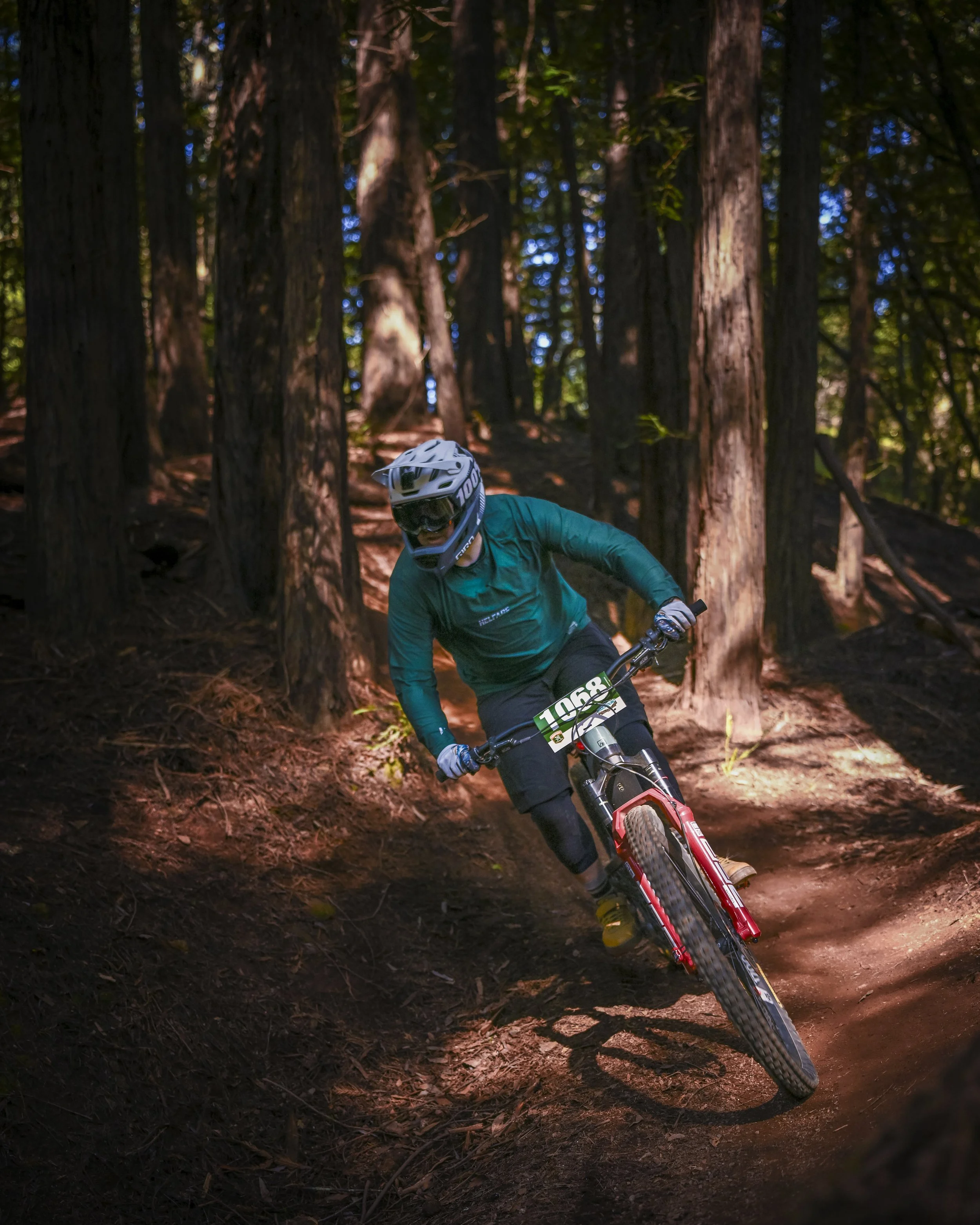 A mountain biker wearing a helmet and blue jacket riding through a forest trail with tall trees and dirt.
