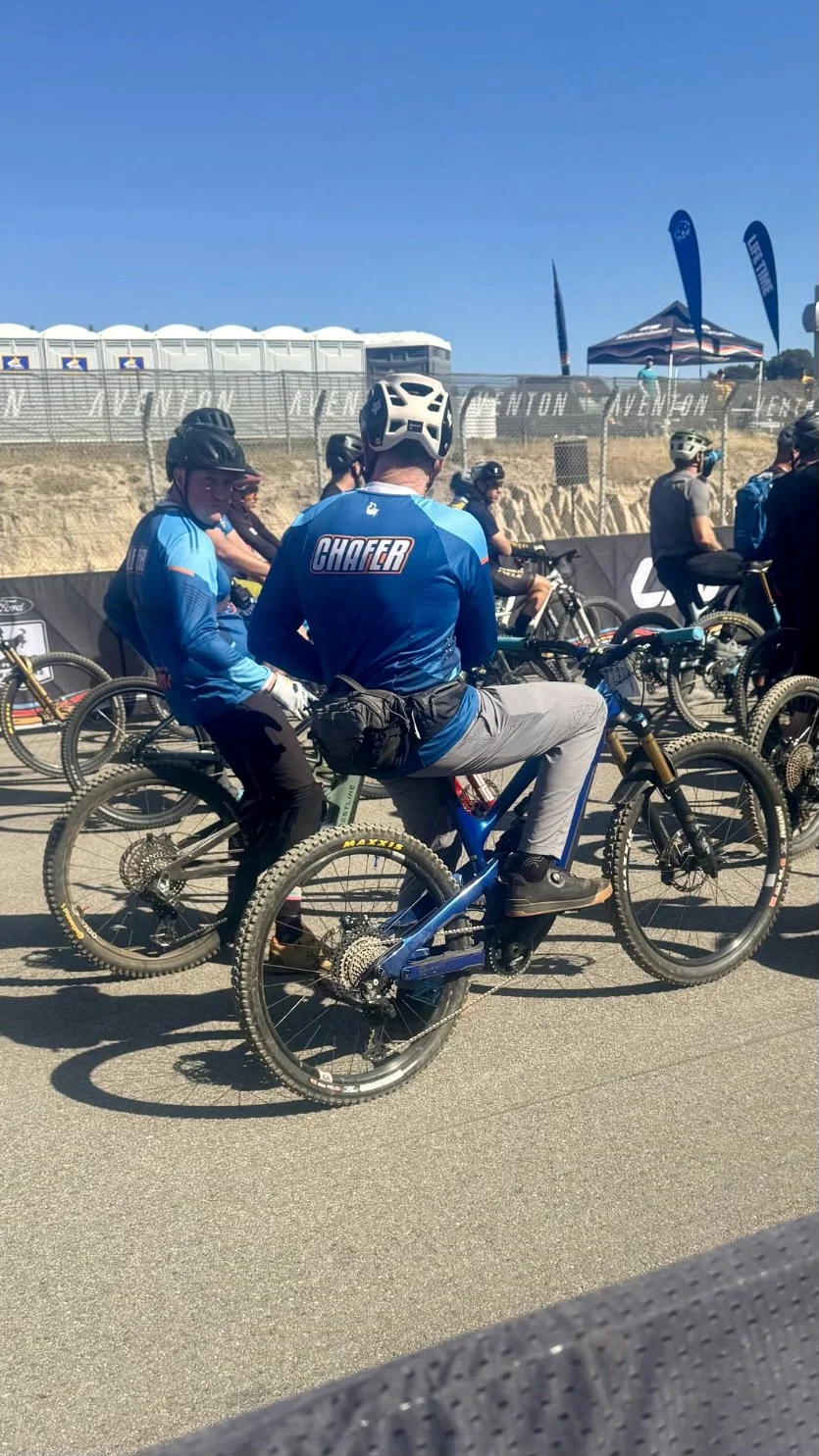 People in cycling gear and helmets sitting on mountain bikes at a cycling event on a sunny day.