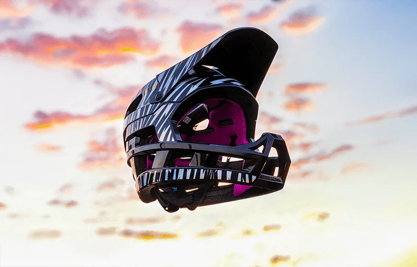 A black and pink bicycle helmet floating in the sky during sunset.