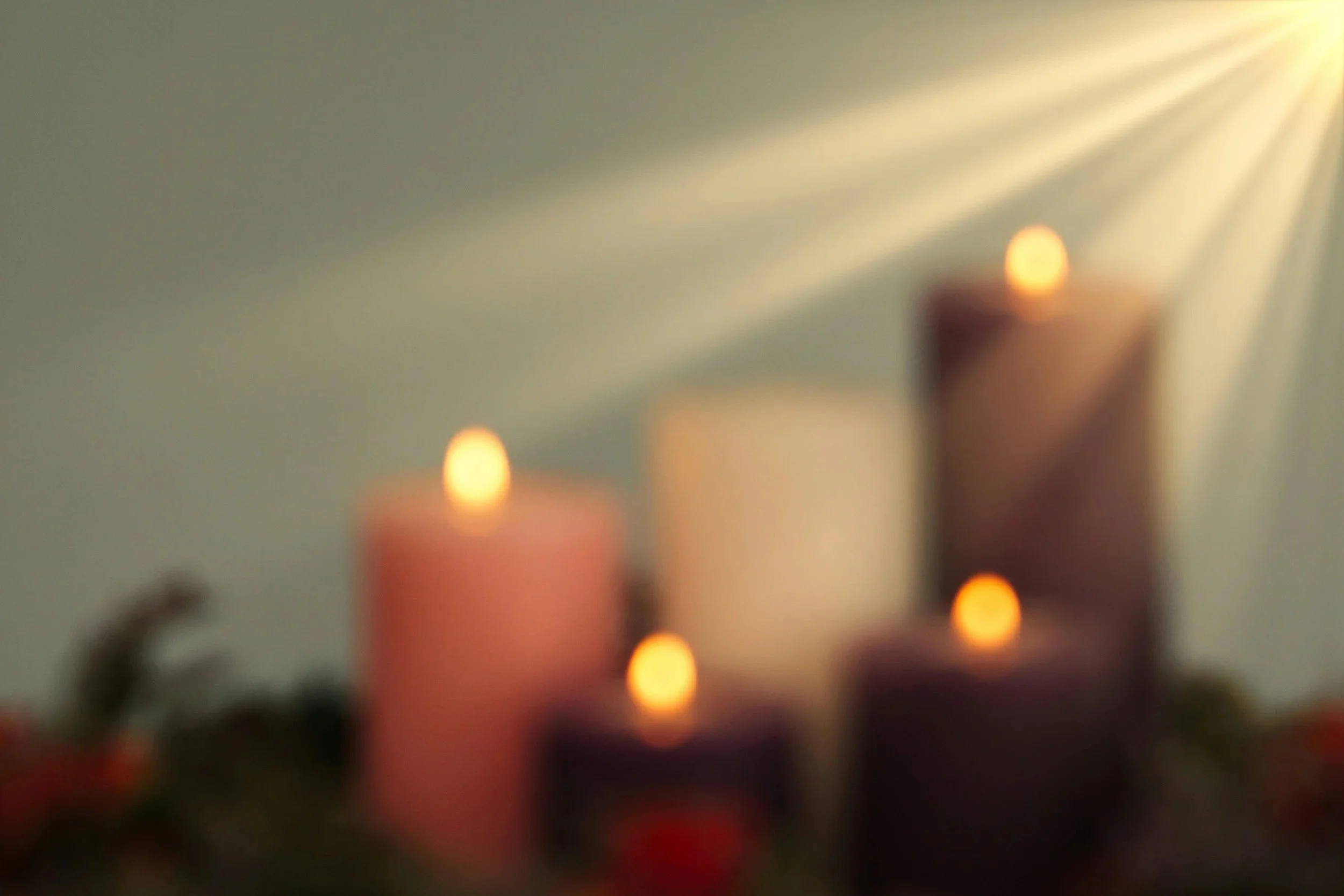 Blurred image showing a row of lit candles with a soft glow, against a neutral background.