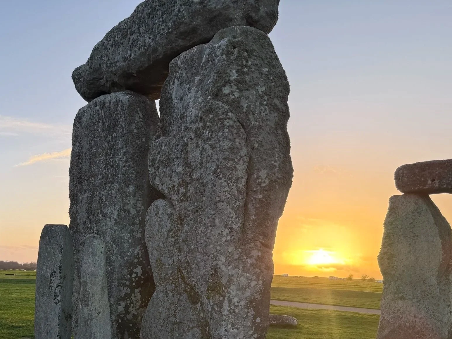 Stonehenge standing stones during sunset with a grassy landscape in the background.