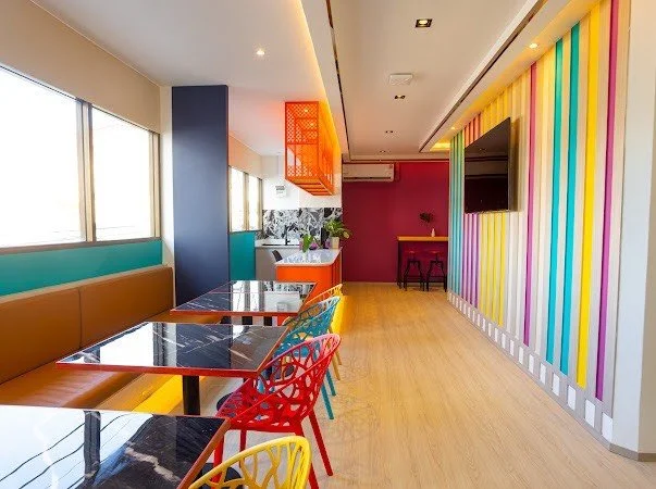 Colorful interior of a modern cafe or restaurant with a row of tables and chairs, vibrant wall decor, and large windows.