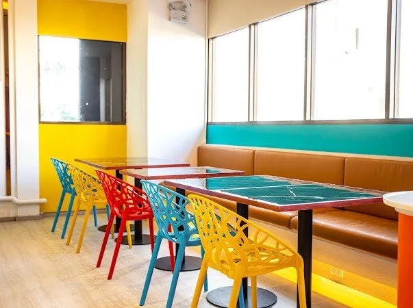 Colorful dining area with multicolored chairs, tables, a long booth seating along windows, and vibrant wall accents.