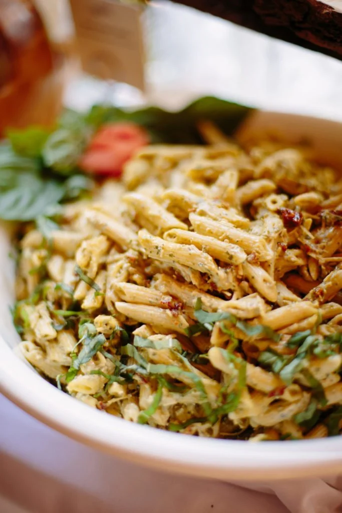 A bowl of pasta salad with shredded chicken, chopped vegetables, and garnished with fresh herbs.