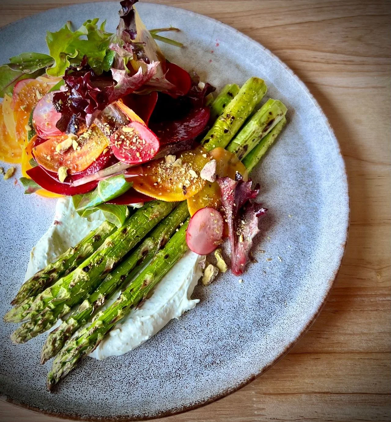 Fresh vegetable salad with asparagus, radishes, cherry tomatoes, mixed greens, and nuts, served on a plate with a creamy spread.