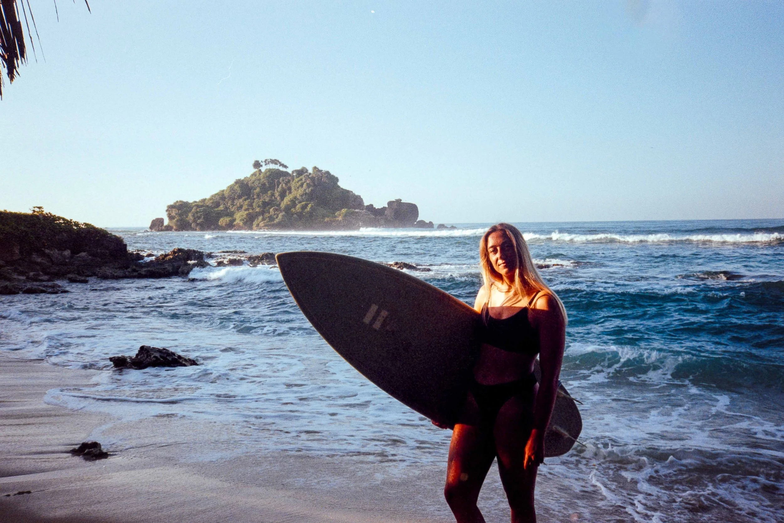 Mary, a solo traveller, holding her surfboard at Devil Rock, Ahangama, Sri Lanka
