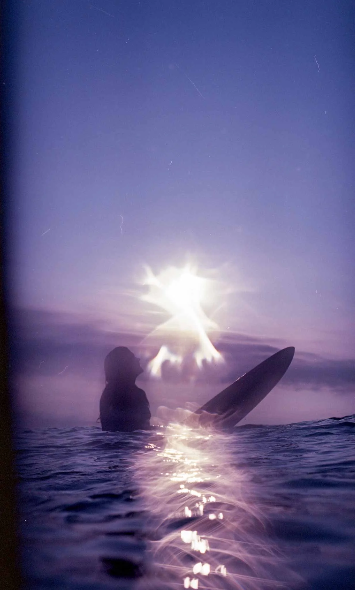surfer girl in the ocean with the sun behind