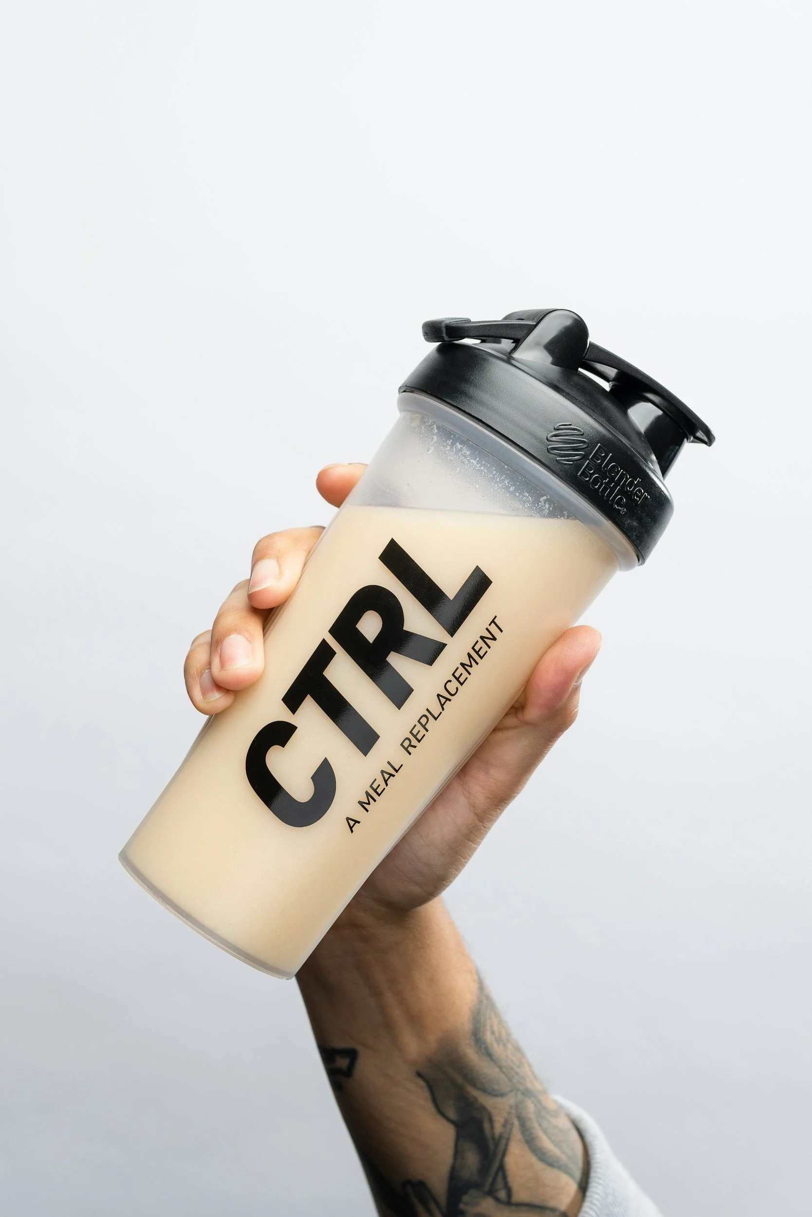 Main tenant une gourde blanche avec un logo noir et le mot 'CITI' écrit dessus. La gourde a un bouchon noir avec un système de fermeture. Arrière-plan blanc, bras tatoué tenant la gourde.