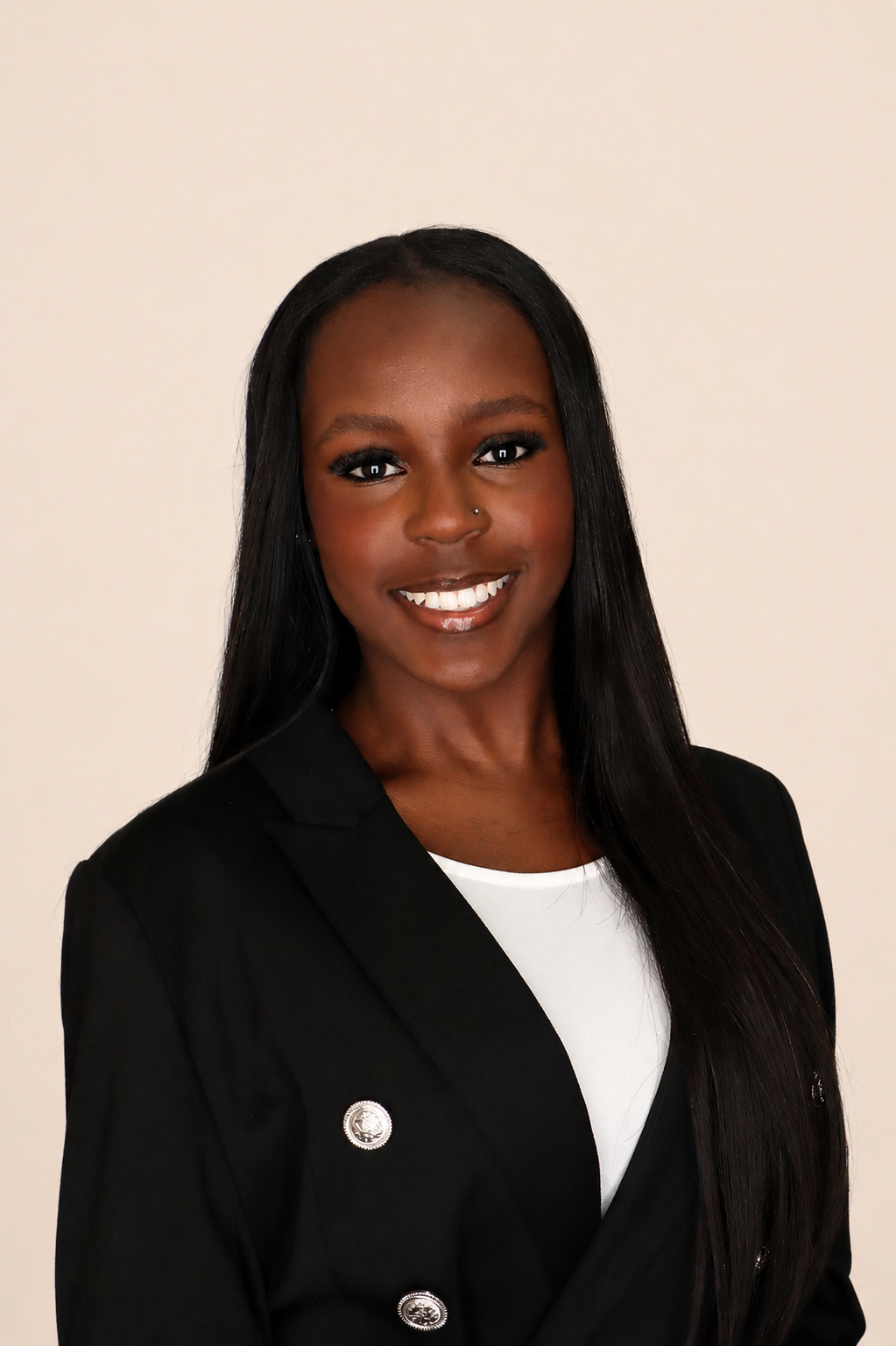 A professional woman with long black hair, wearing a black blazer with silver buttons and a white top underneath, smiling against a neutral background.