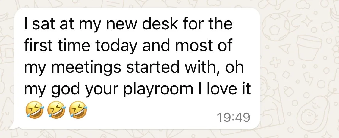 Text message on a chat screen that reads: 'I sat at my new desk for the first time today and most of my meetings started with, oh my god your playroom I love it 😂😂😂'.