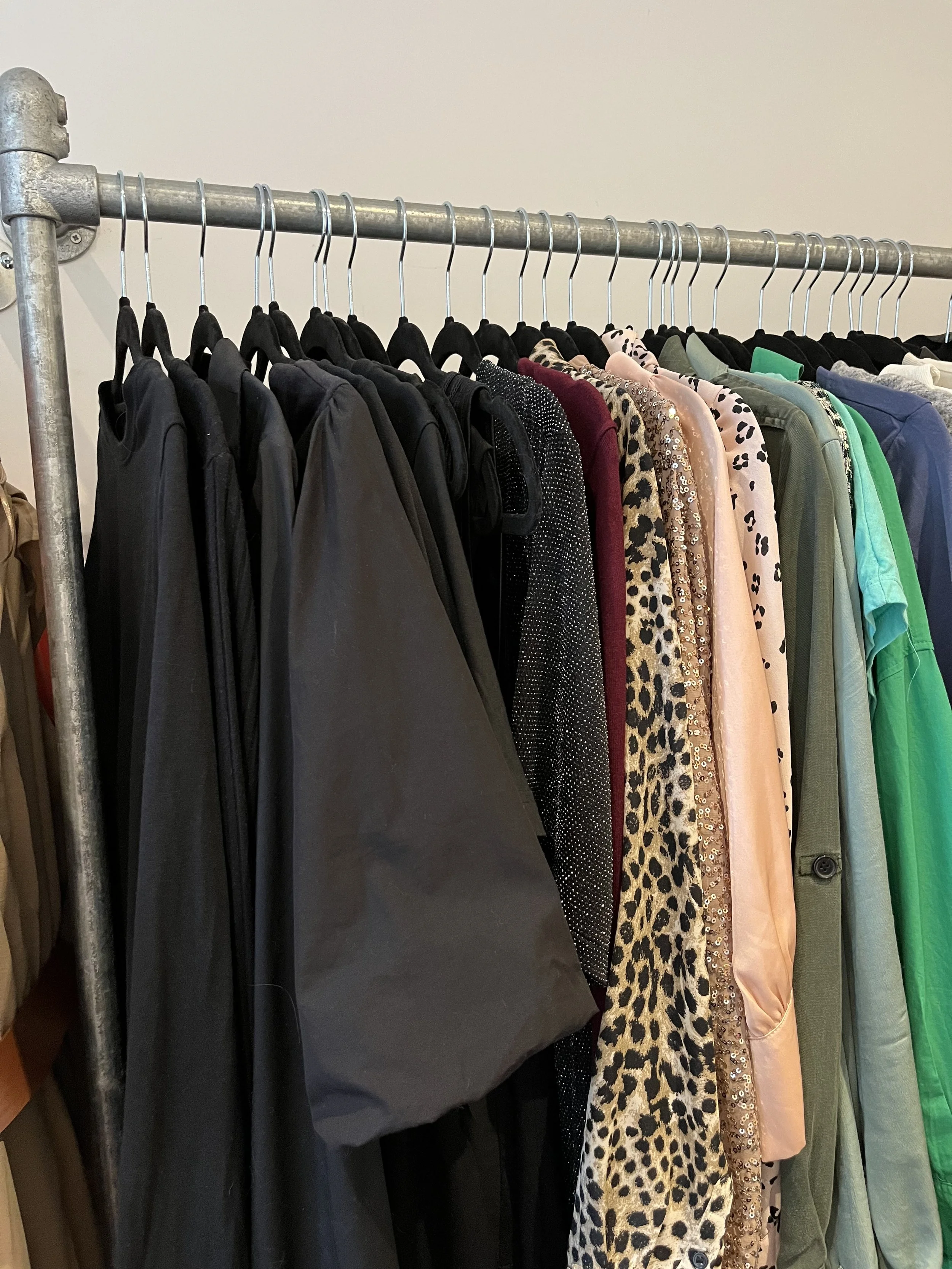 a rail of different coloured clothes hung on black hangers