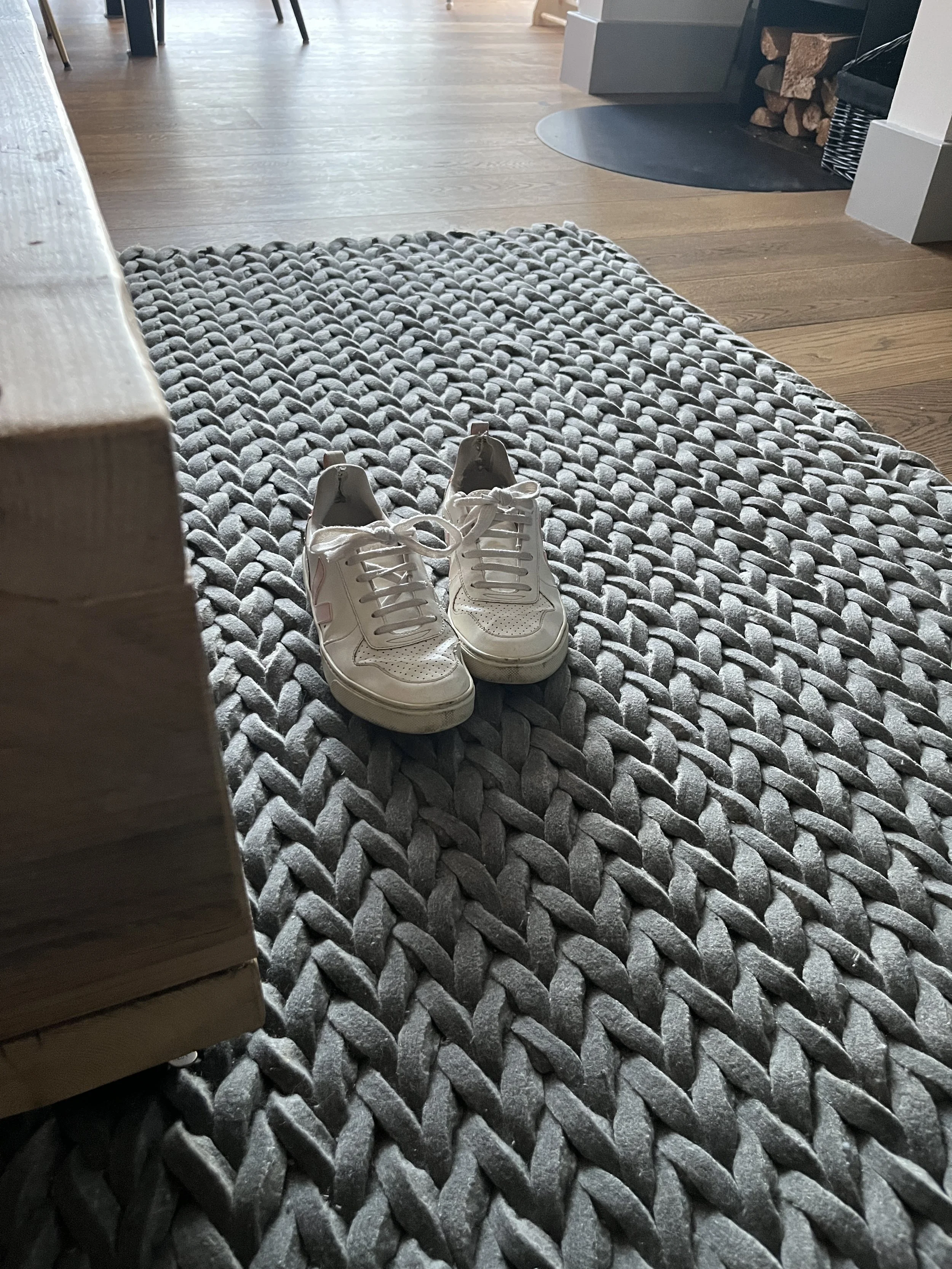 A pair of white sneakers on a gray textured rug inside a home with wooden flooring and modern furniture.