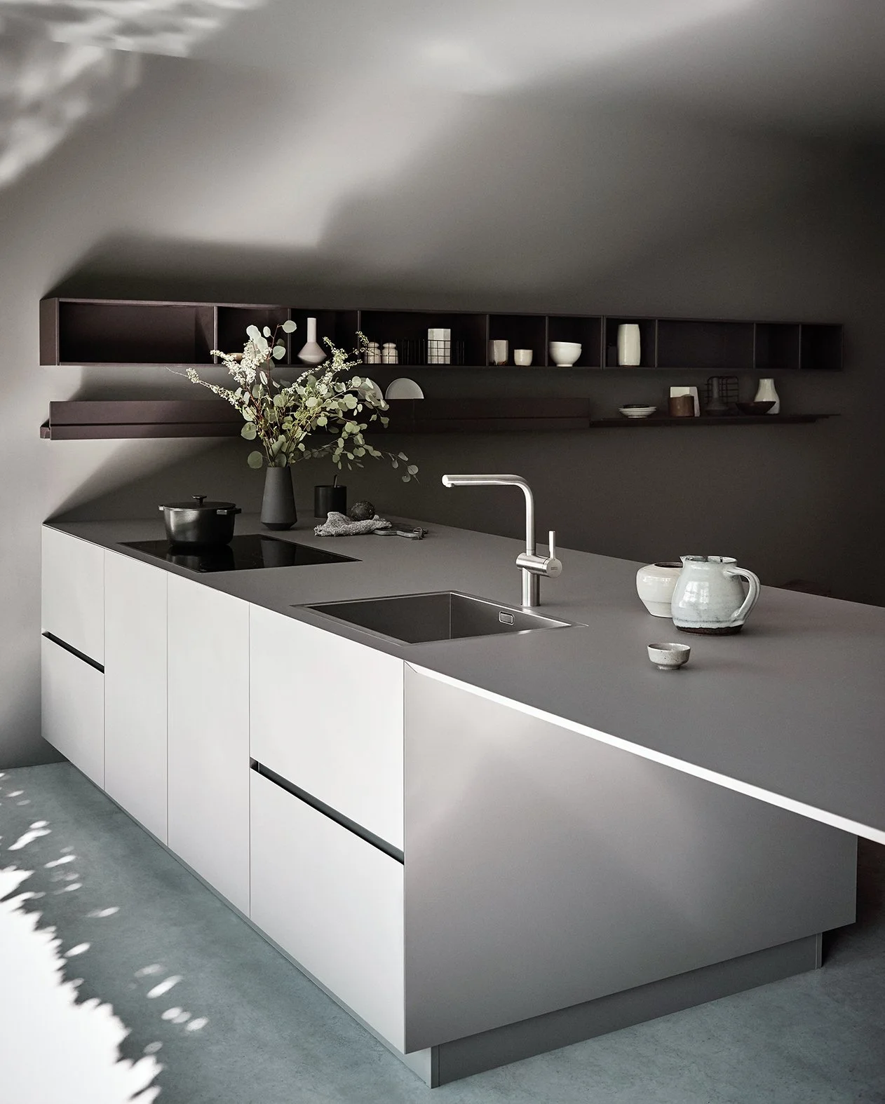 Moderne Kücheninsel mit weißem Unterschrank, grauer Arbeitsplatte, Spüle und Wasserhahn, Dekoration mit Keramiktassen, Vase mit Zweigen und geschmackvollen Geschirrstücken, schwarze offene Wandregale mit Geschirr und Dekorationsobjekten, helles Rauml
