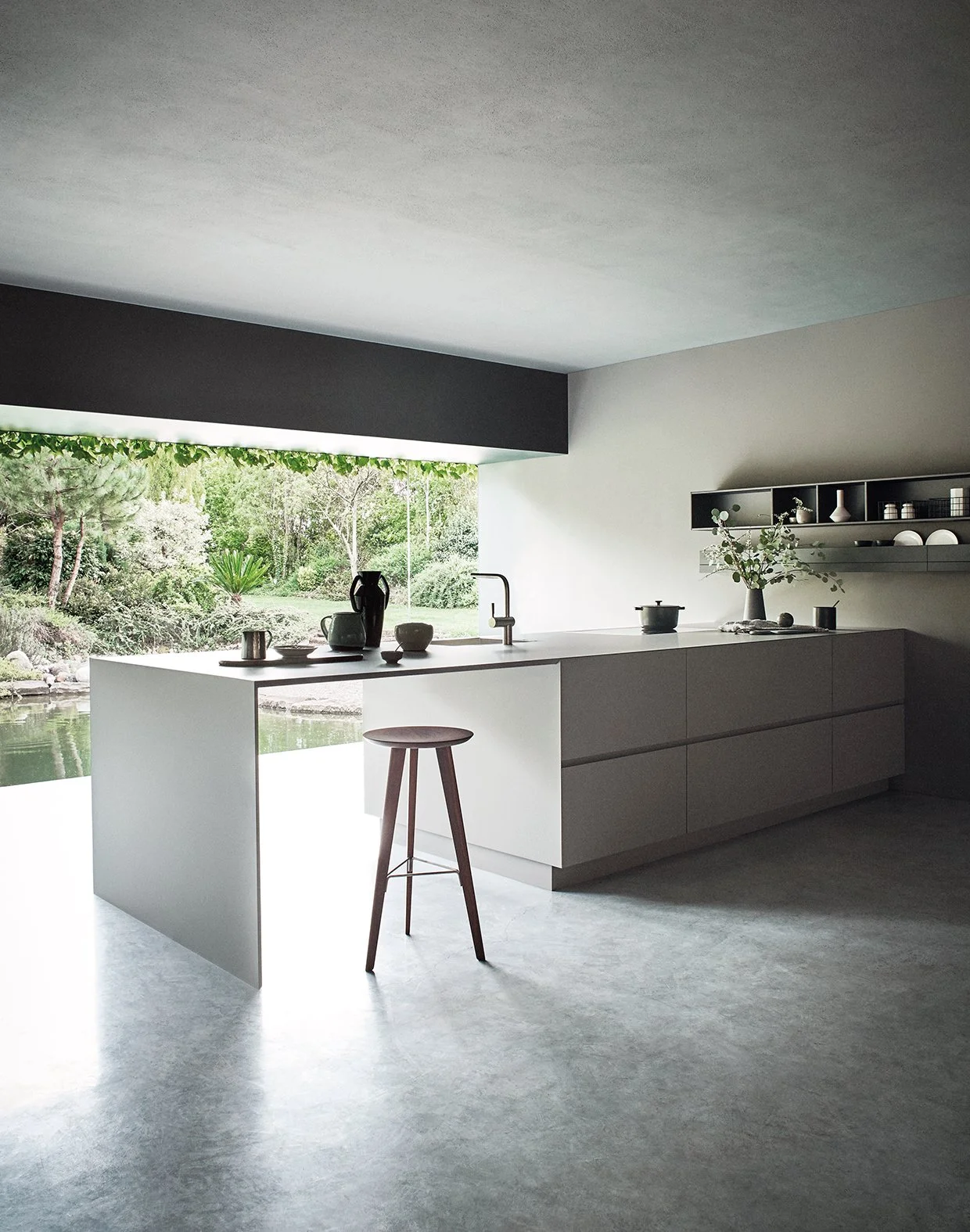 Moderne, minimalistische Küche mit weißen Schränken, Blick auf einen Garten durch eine große Fensterwand, einige Küchenutensilien und Dekorationen auf der Arbeitsfläche, Holsth genau