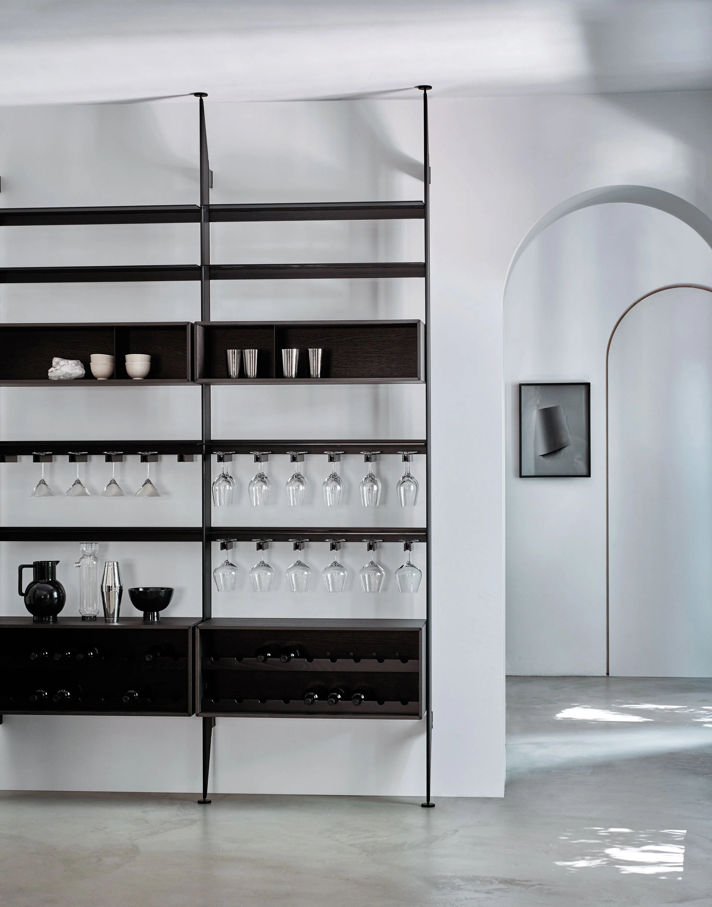 Ein moderner schwarzer Bar-Schrank mit Gläsern, Tassen und Dekorationsgegenständen in einem minimalistischen, hellen Raum.