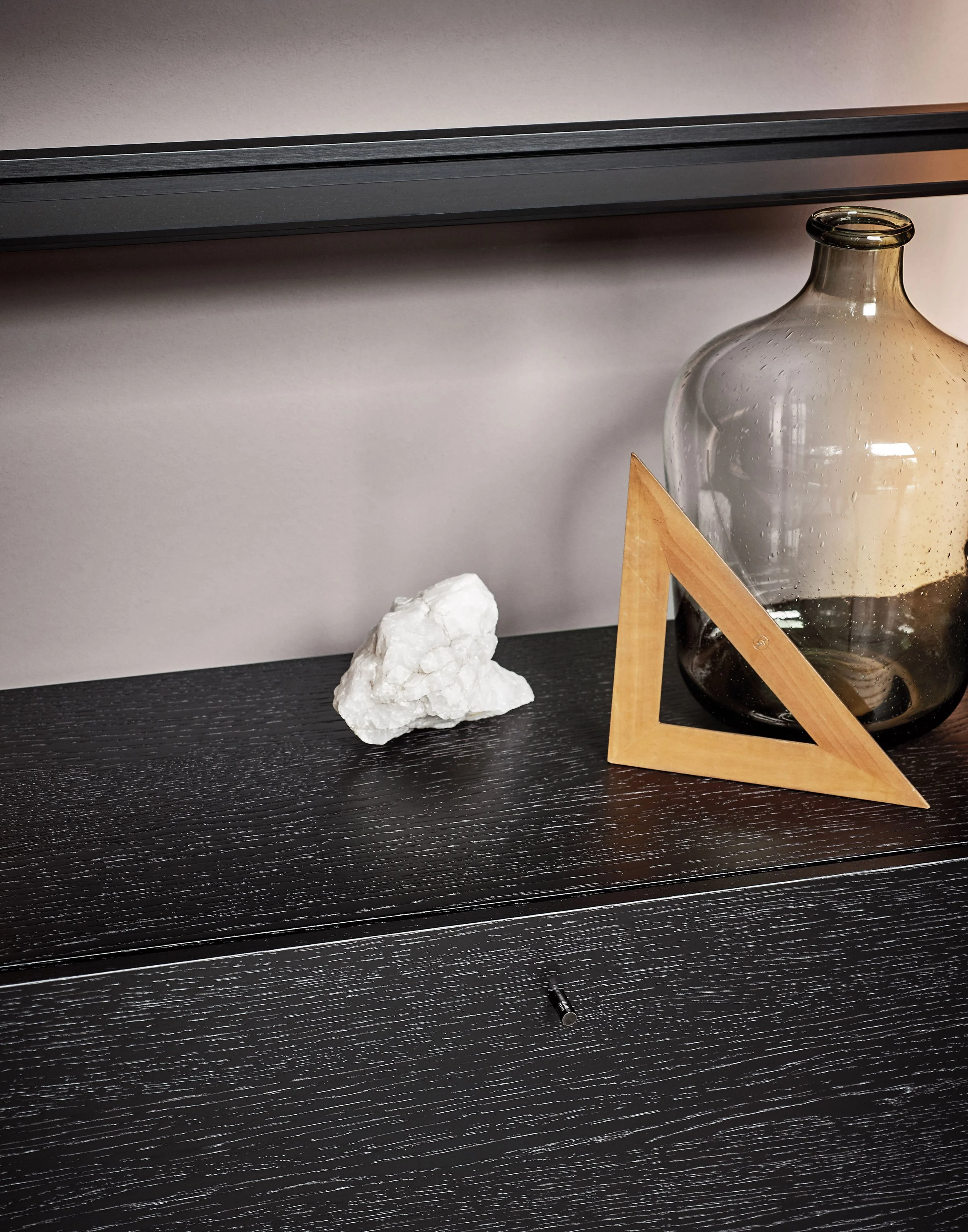 Ein Tisch mit schwarzer Holzoberfläche, auf dem eine weiße Gipsfigur, eine Glaskaraffe und eine Holzskulptur stehen, sowie ein schwarzer Kugelschreiber im Vordergrund.