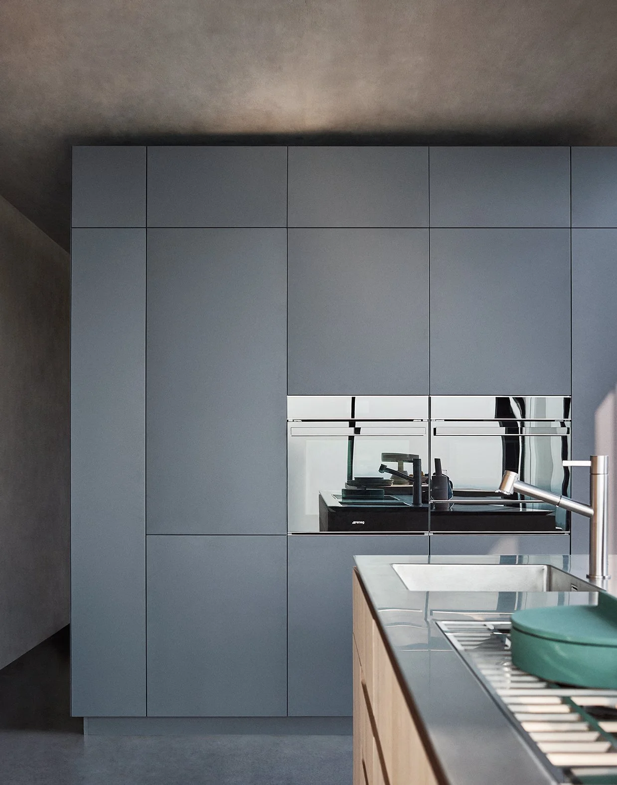 Moderne Küche mit blauen Schränken, integrierter Backofen, Spüle am Holzarbeitsblock, und grüner Aufbewahrungsbox auf der Theke.