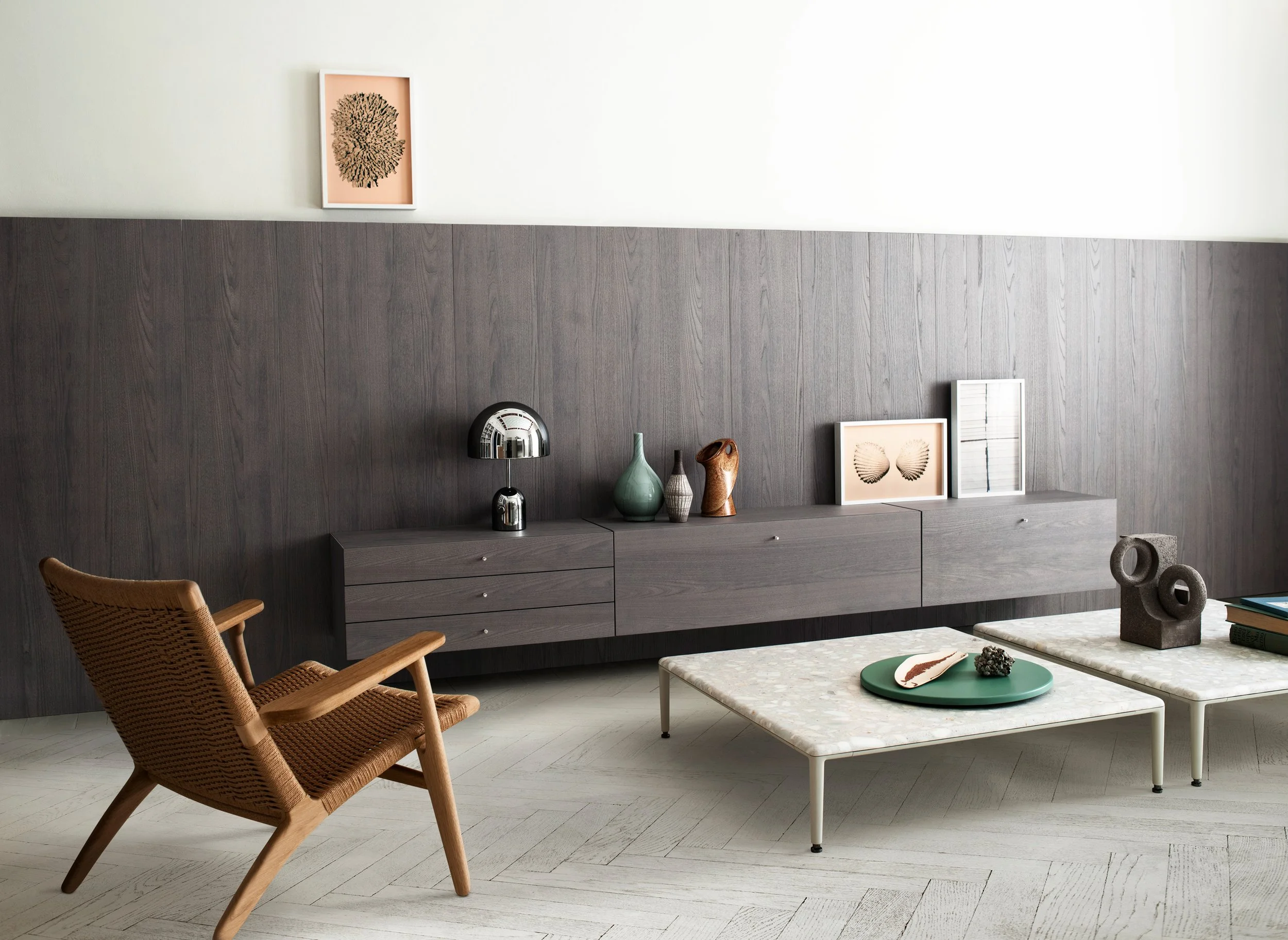 Moderner Wohnraum mit grauer Wandvertäfelung, Boho-Dekor und zwei Holzstühlen, helles Marmortisch mit Dekoration und Büchern, Wanddeko-Bilder, Tischlampe mit metallischem Schirm.