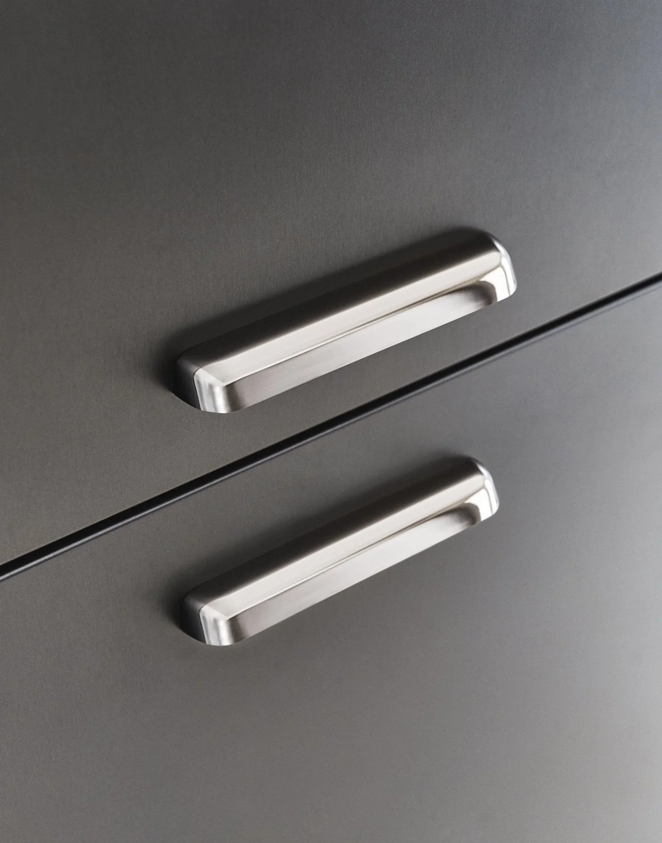 Nahaufnahme von zwei eleganten silbernen Griffen an einem modernen grauen Schrank. Die hochwertigen Metallgriffe und das minimalistische Möbeldesign verleihen der Inneneinrichtung einen stilvollen und modernen Charakter mit zeitloser Eleganz.