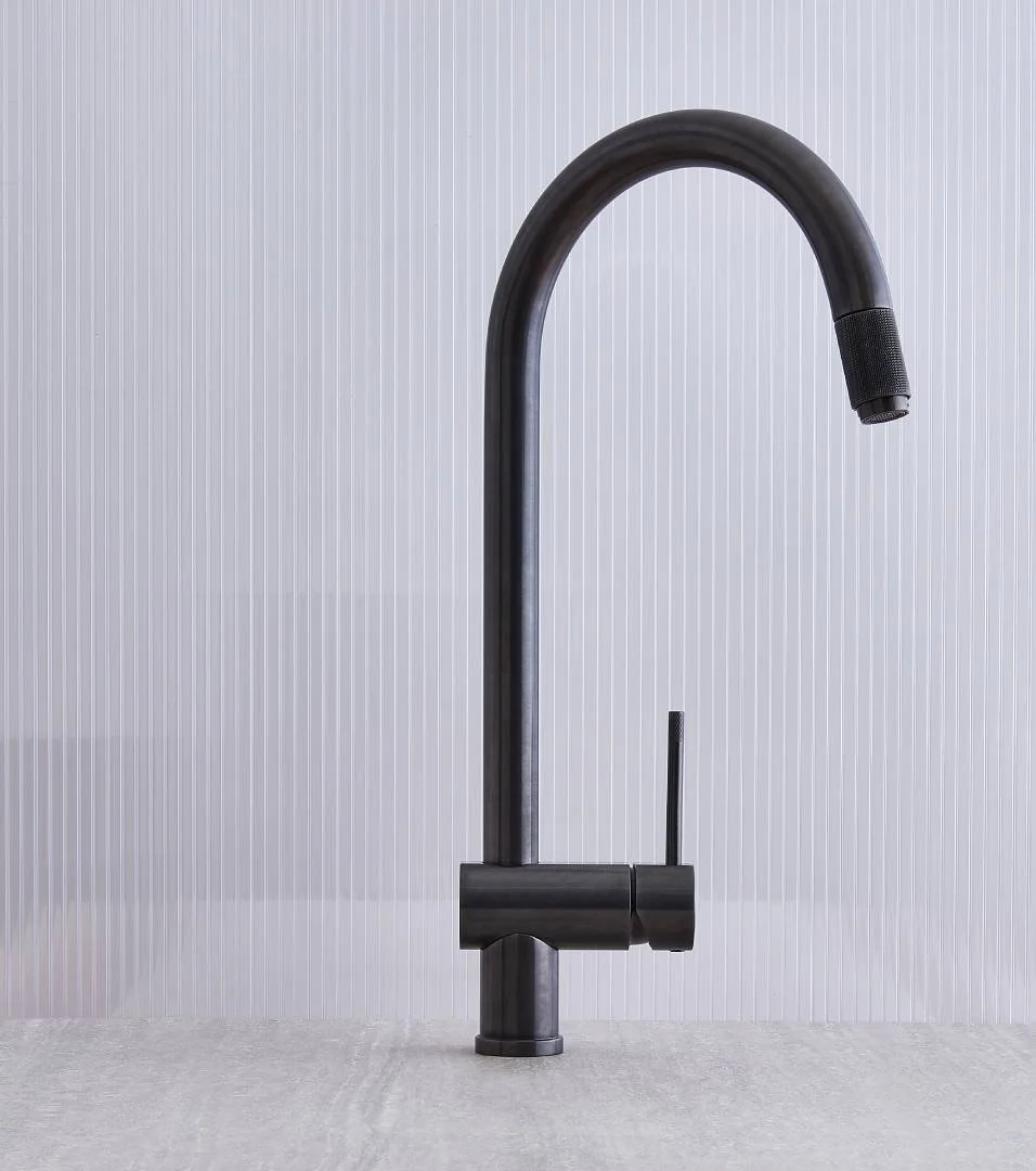 Schwarzer Wasserhahn mit integriertem Y-Auslauf vor einer hellen, vertikal linierten Wand.