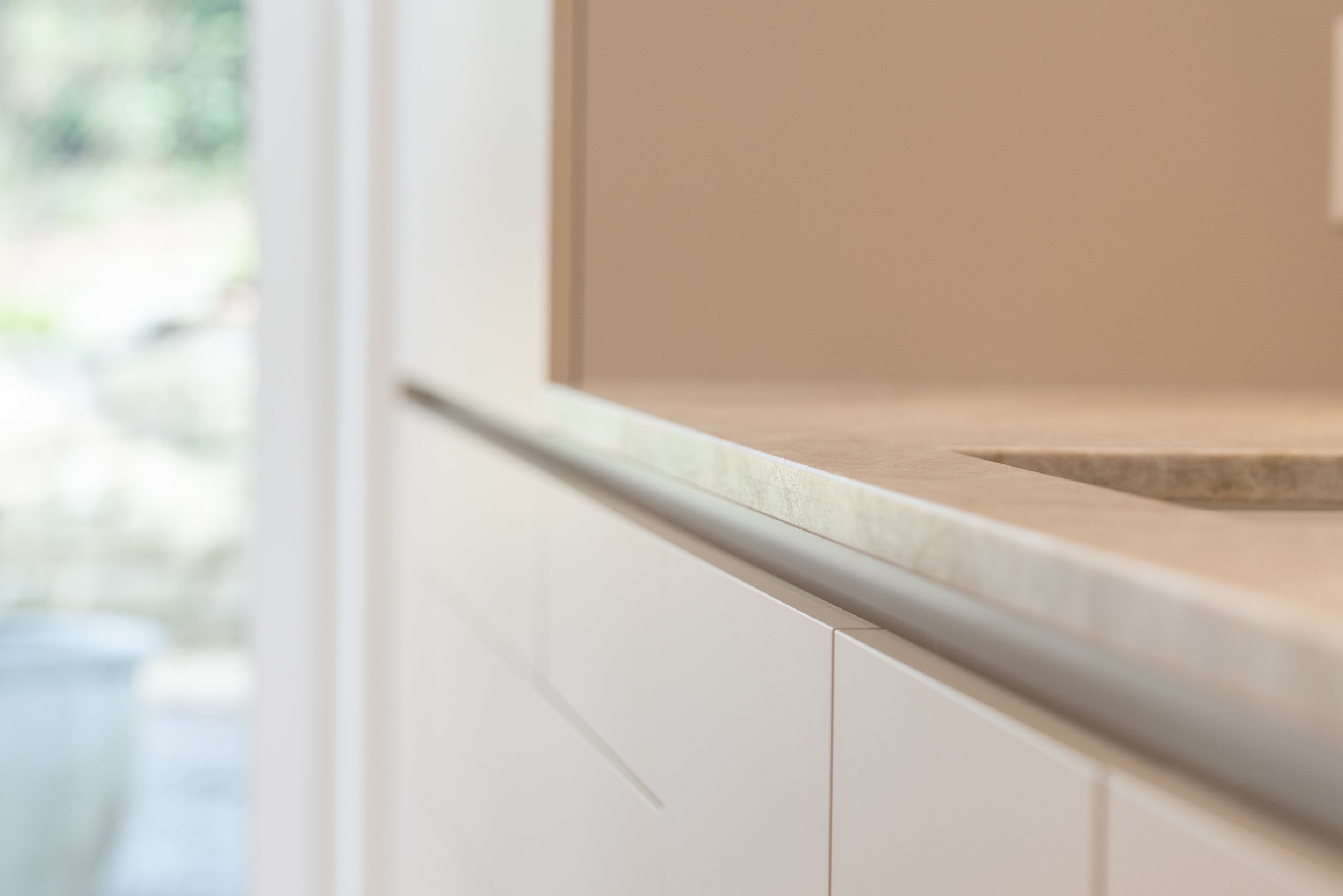 Nahaufnahme einer Küchenarbeitsplatte aus Marmor mit Spüle, unscharfer Hintergrund mit Glas und Pflanzen