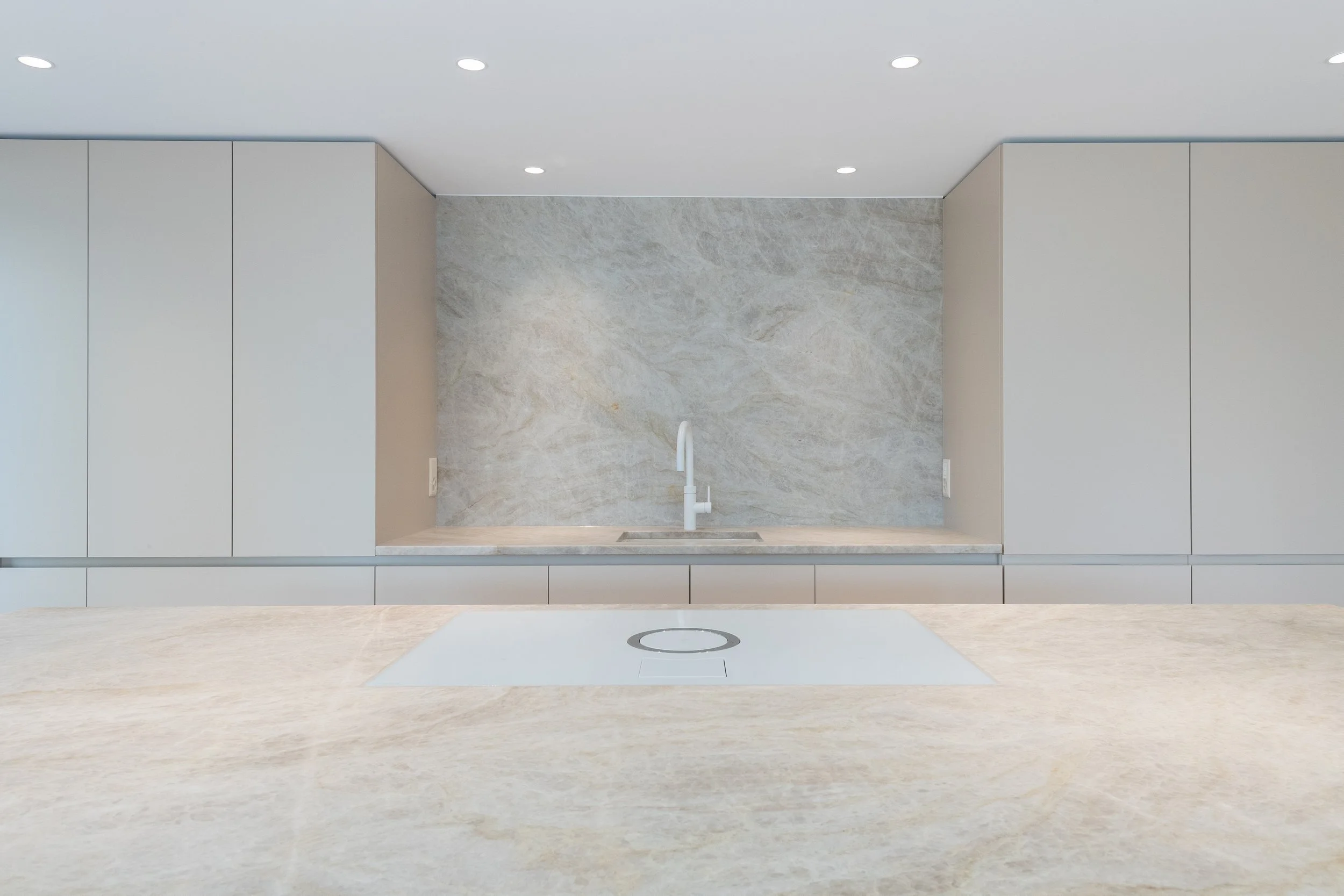 Moderne, minimalistische Küchenansicht mit hellem Steinwerkzeug, Waschbecken, Wasserhahn und integriertem Induktionskochfeld.