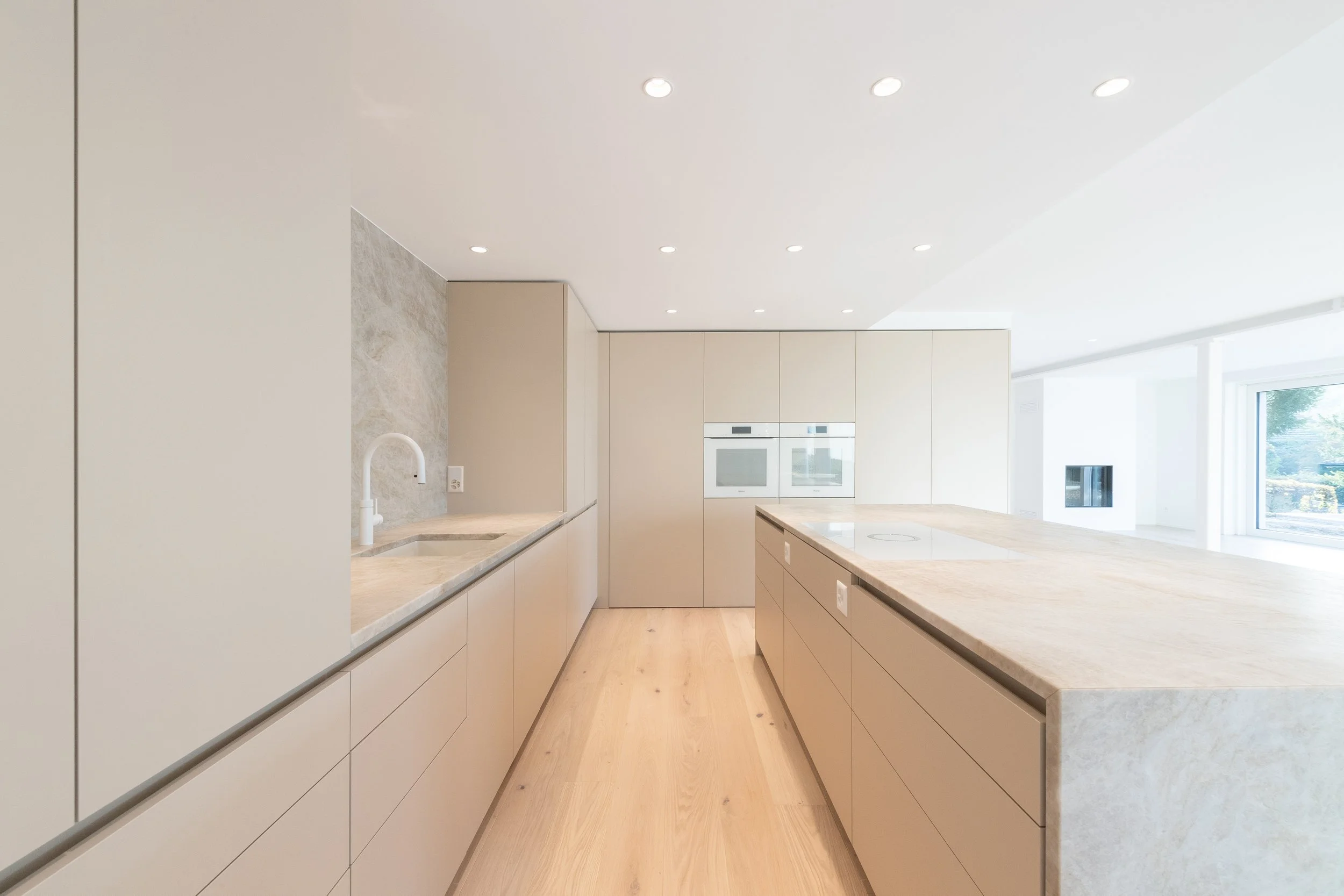 Moderne, minimalistische Küche mit weißen Schränken, Holzboden und großem Kücheninsel.