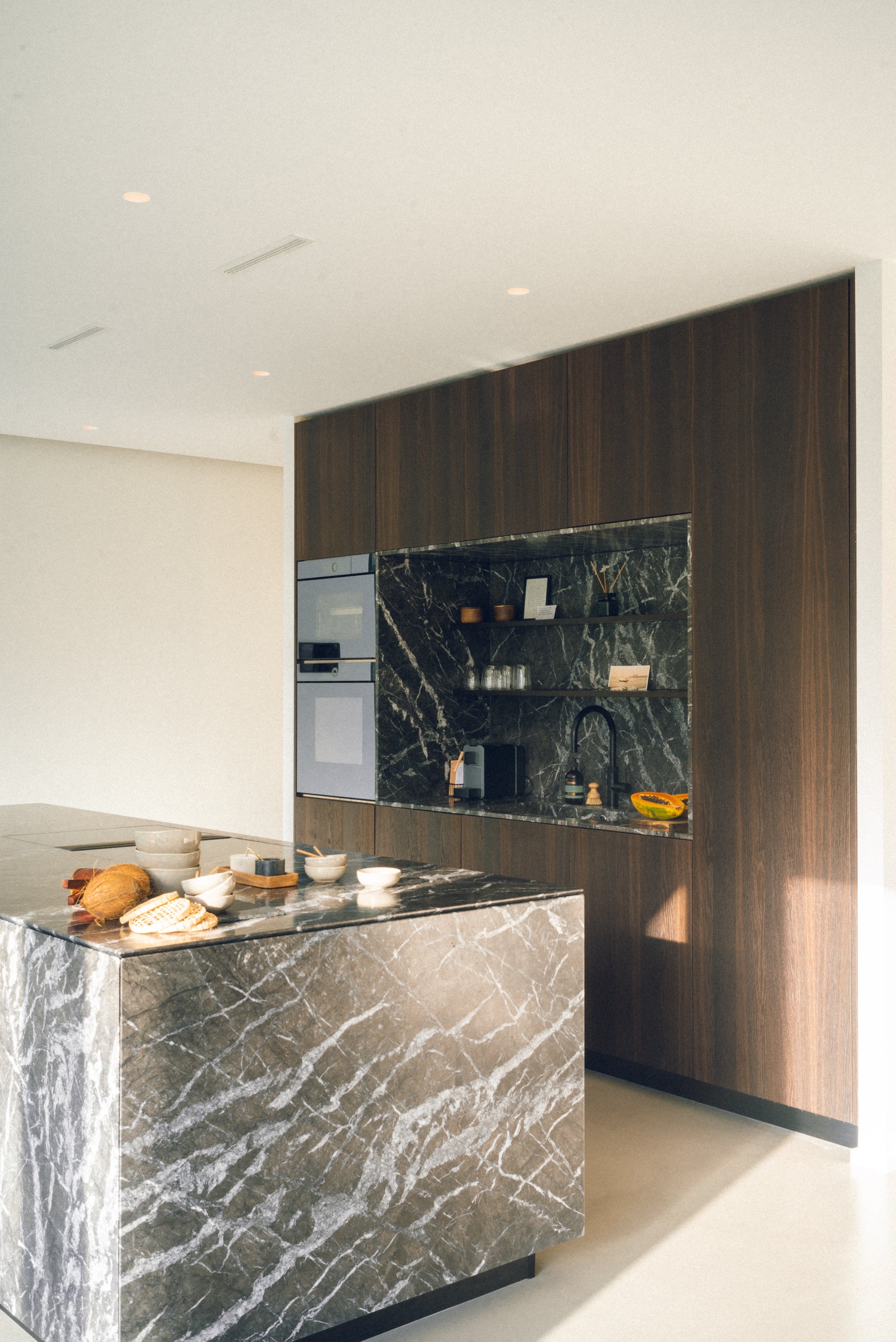 Moderne Küche mit schwarzer Marmor-Arbeitsplatte und Wand, Holzschränken, Küchenutensilien und Dekoration auf dem Inselblock.