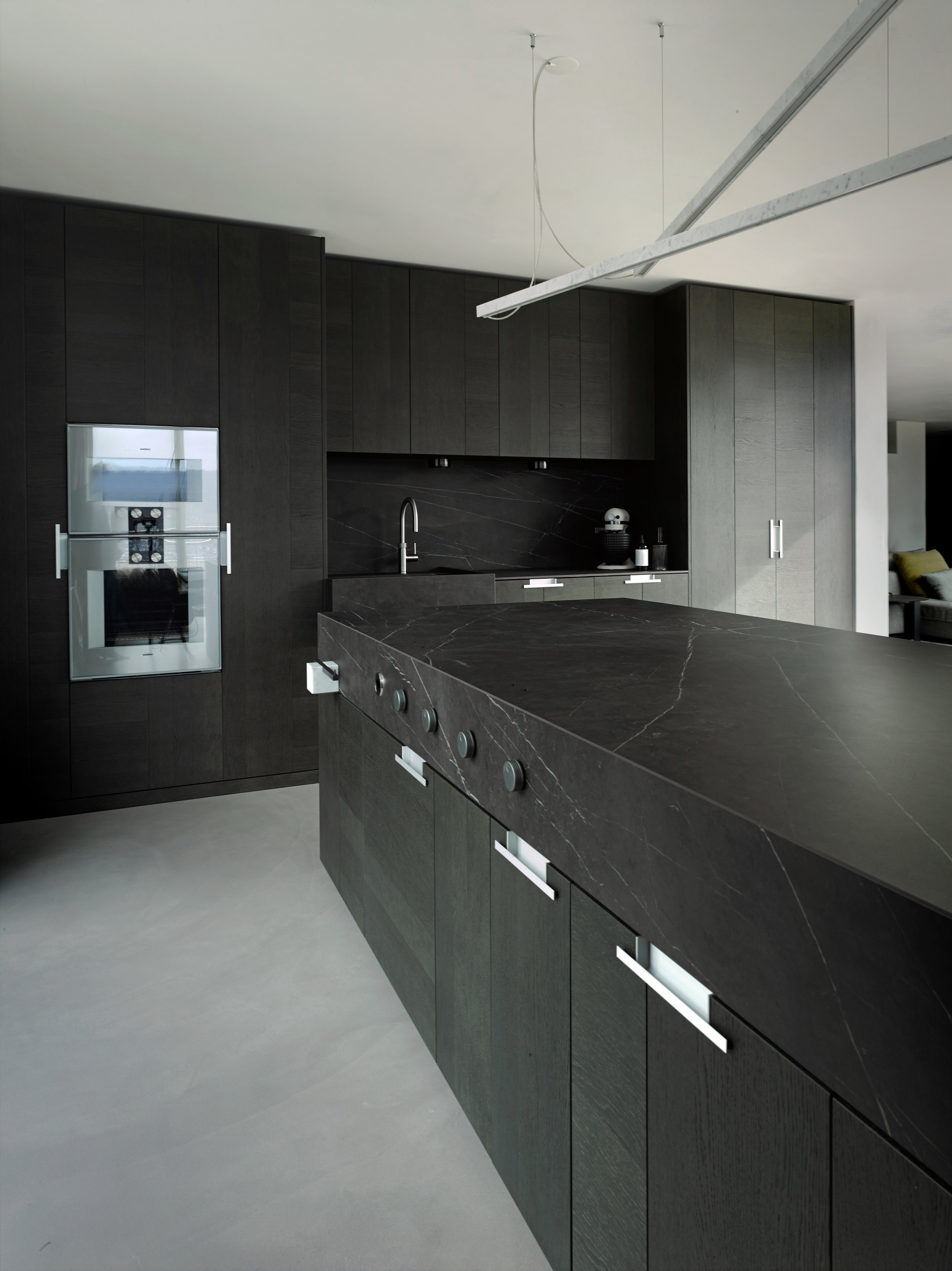 Moderne schwarze Küche mit schwarzen Holzschränken, schwarzen Marmor-Arbeitsflächen und eingebauten Küchengeräten in einer offenen Wohnraumgestaltung.