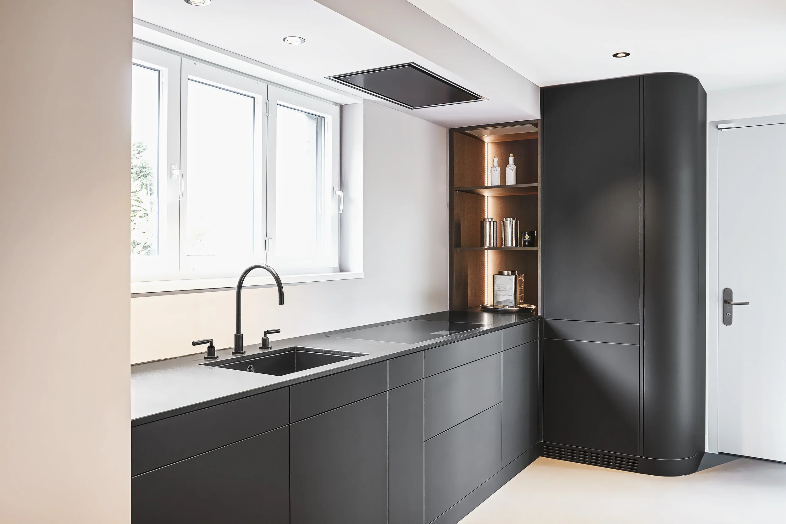 Moderne Küche mit schwarzen Schränken, einem schwarzen Wasserhahn, einer weißen Wand, einer großen Fensterfront und einer stilvollen schwarzen Küchenschranknische mit geöffneten Regalen