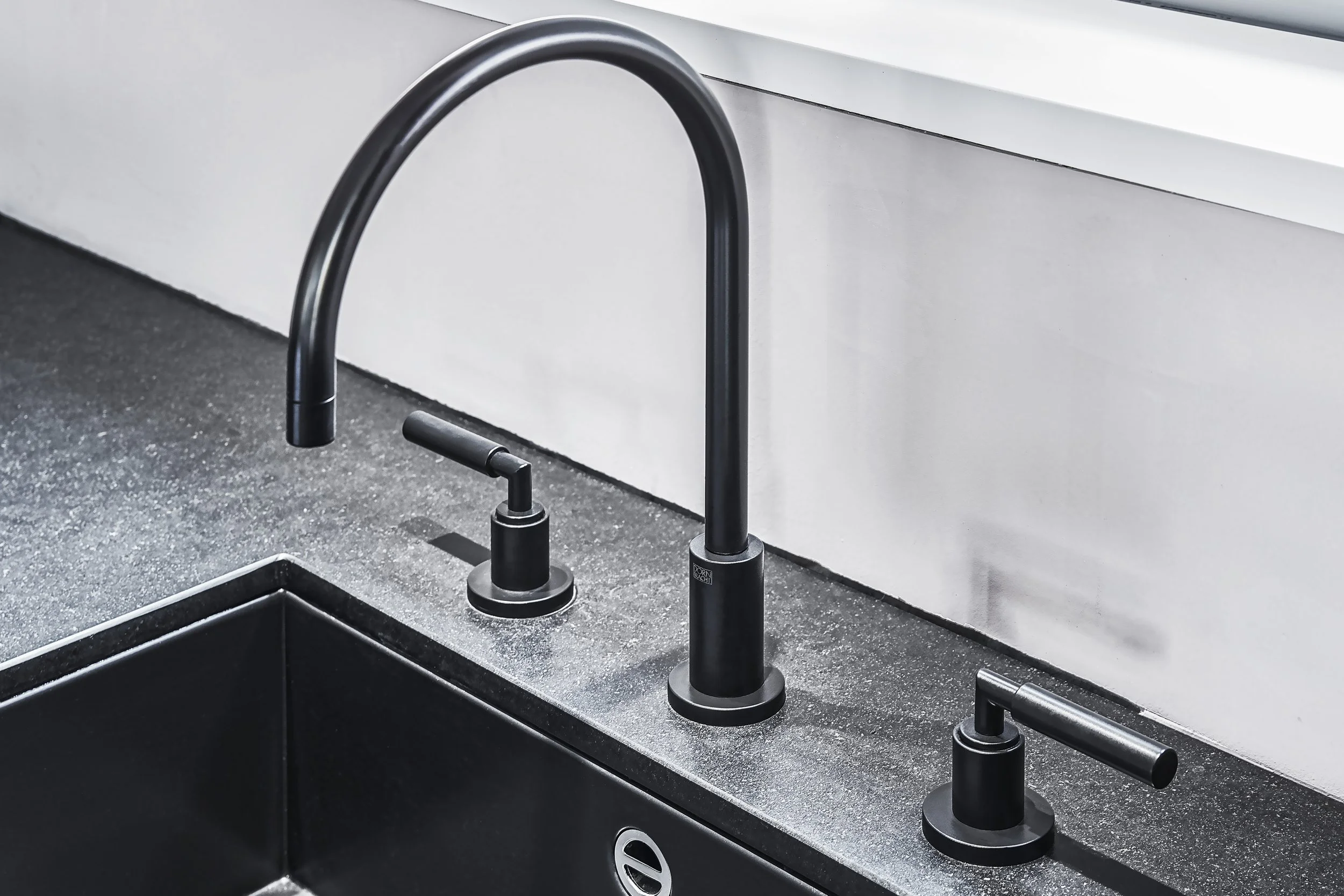 Schwarzer Küchenhahn und zwei Wasserhähne auf grauer Arbeitsplatte in einer modernen Küche.