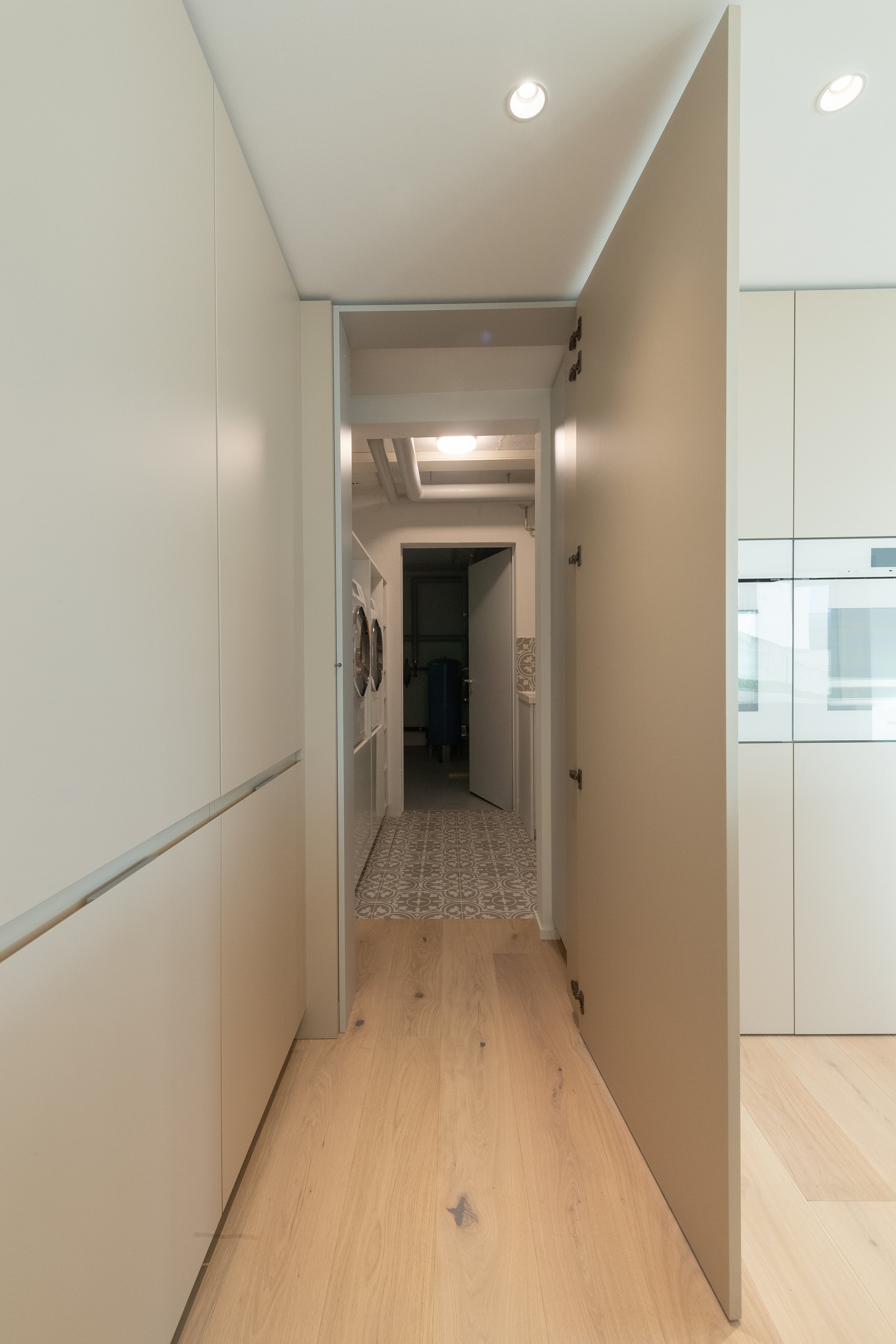Ein offener Türrahmen in einer modernen Wohnung, Blick in einen Flur mit Waschmaschinen, einer Tür und einem Boden mit gemusterten Fliesen.