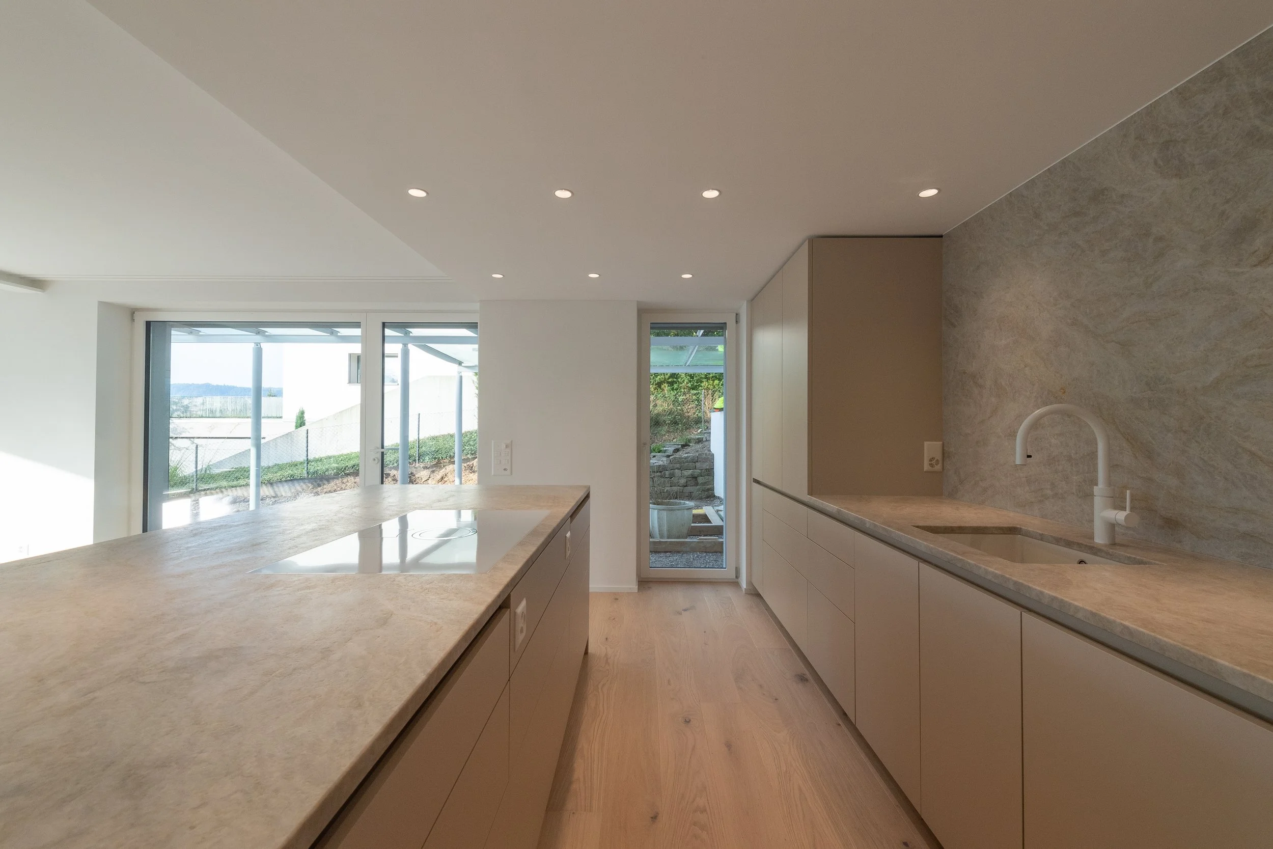 Moderne Küche mit beige Arbeitsplatten, weißen Schränken, einem Waschbecken und einer Tür, die nach draußen führt.